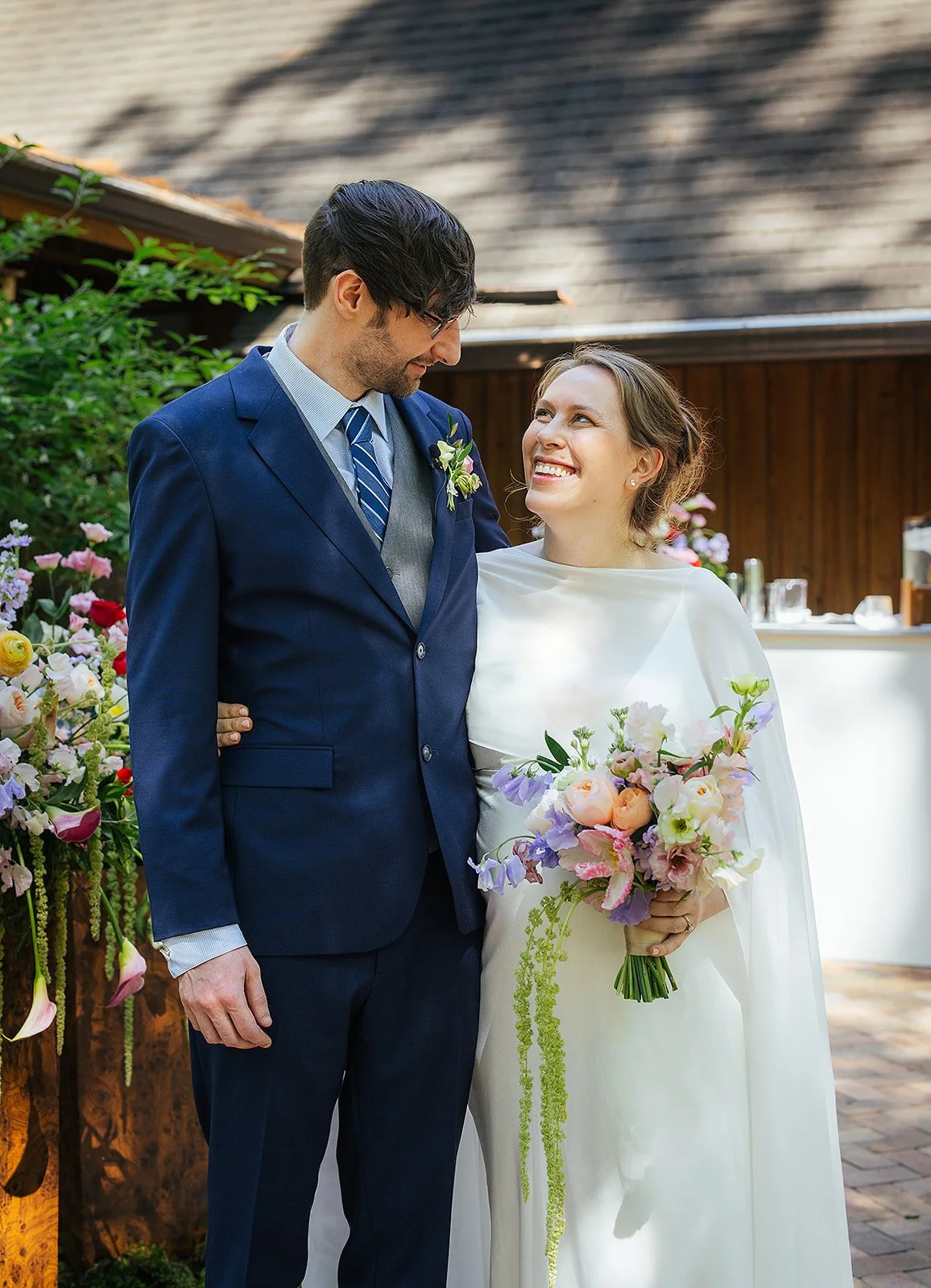 Bride and groom share a joyful portrait moment surrounded by colorful spring flowers at their outdoor wedding ceremony, Durham NC