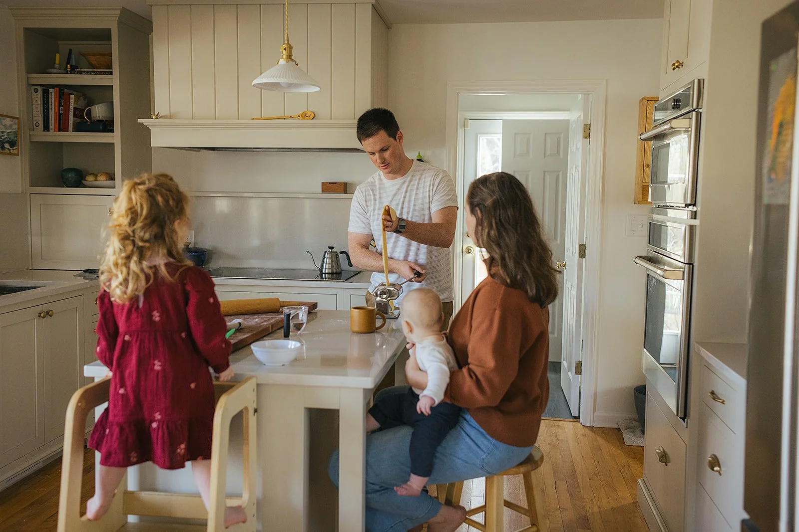 Dad pours tea while family gathers in kitchen during Durham in-home lifestyle family photography session