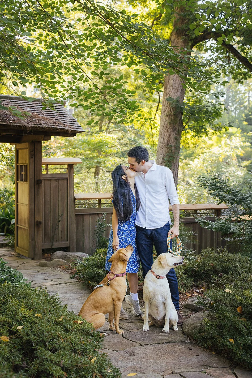 A couple kissing while walking their dogsafter their surprise engagement during a photoshoot at Duke Gardens in Durham, NC