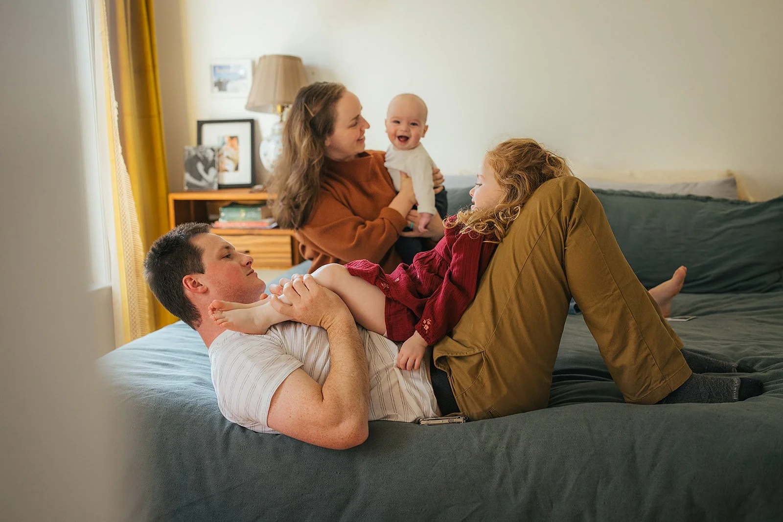 Family of four laughing and playing together on bed during Durham lifestyle family photography session