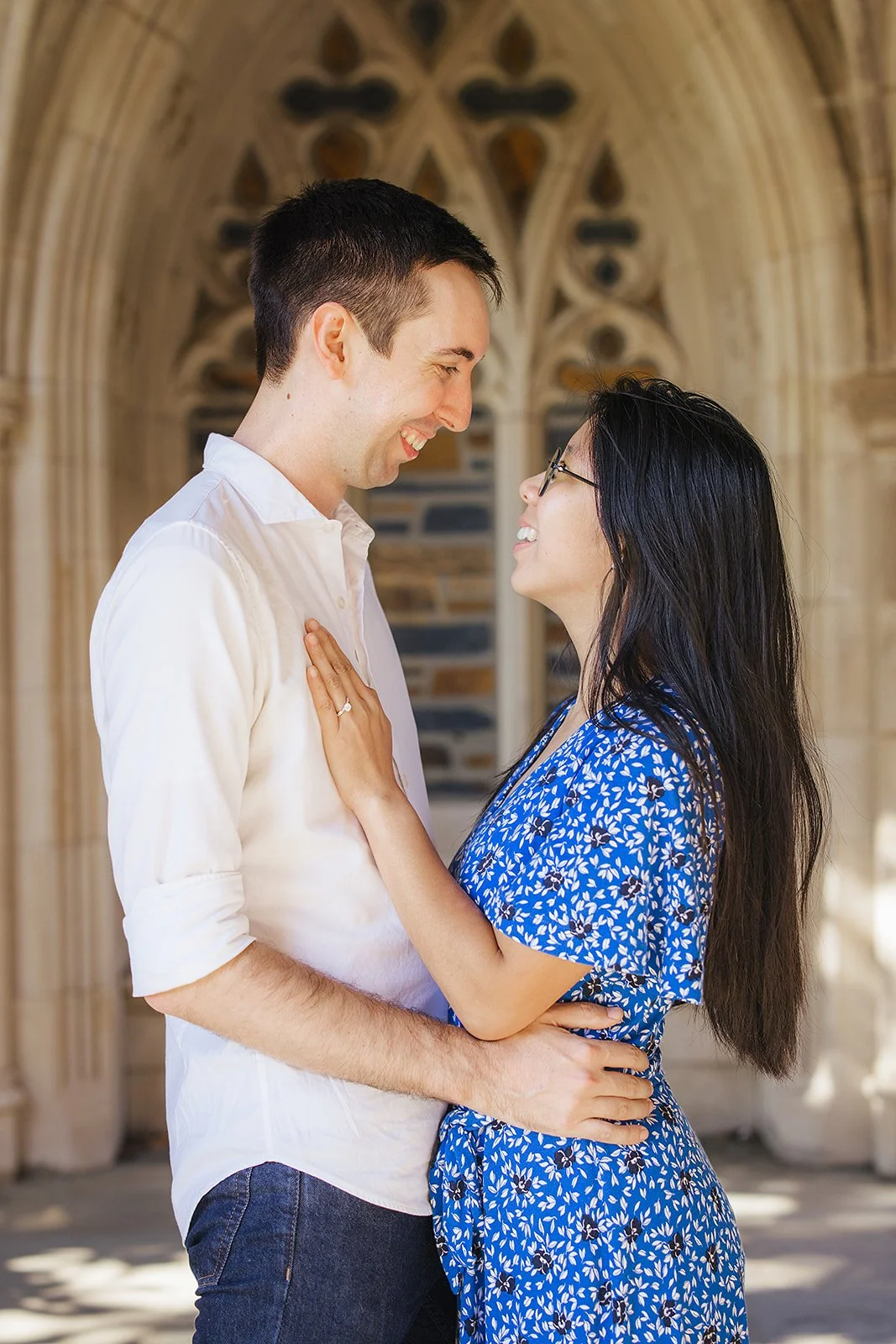 A couple smiles at each other showing off the engagement ring after their surprise engagement during a photoshoot at Duke Gardens in Durham, NC