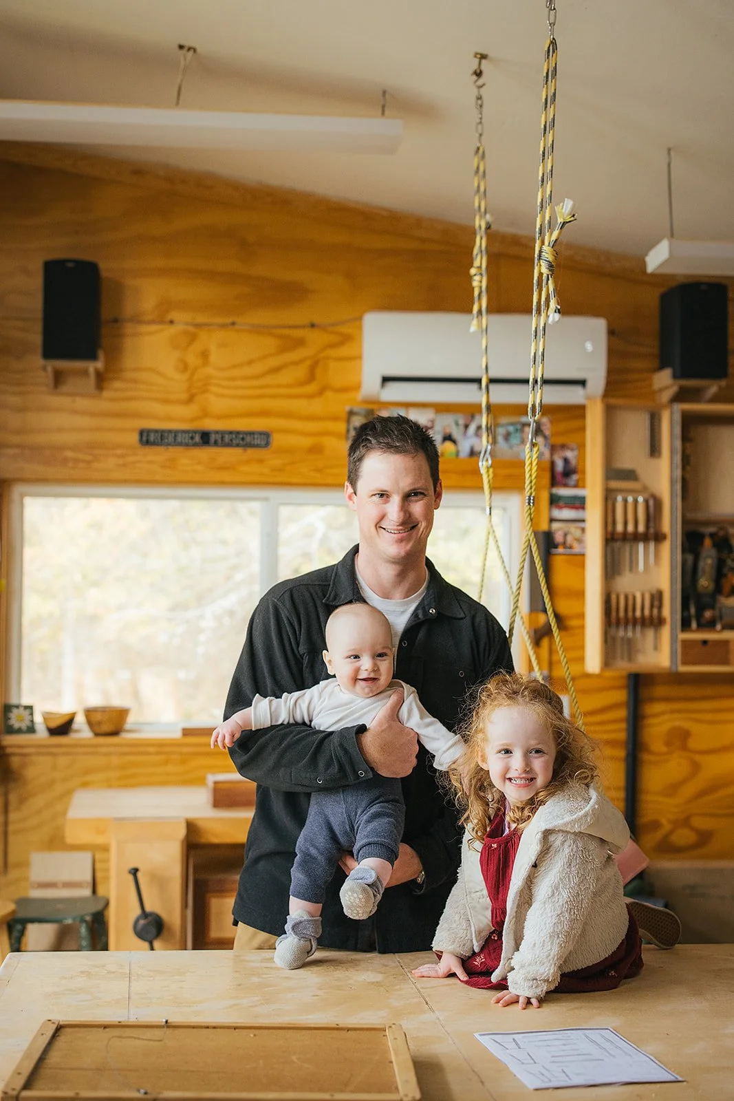 Dad with baby and toddler daughter in his woodworking shop during Durham lifestyle family photography session