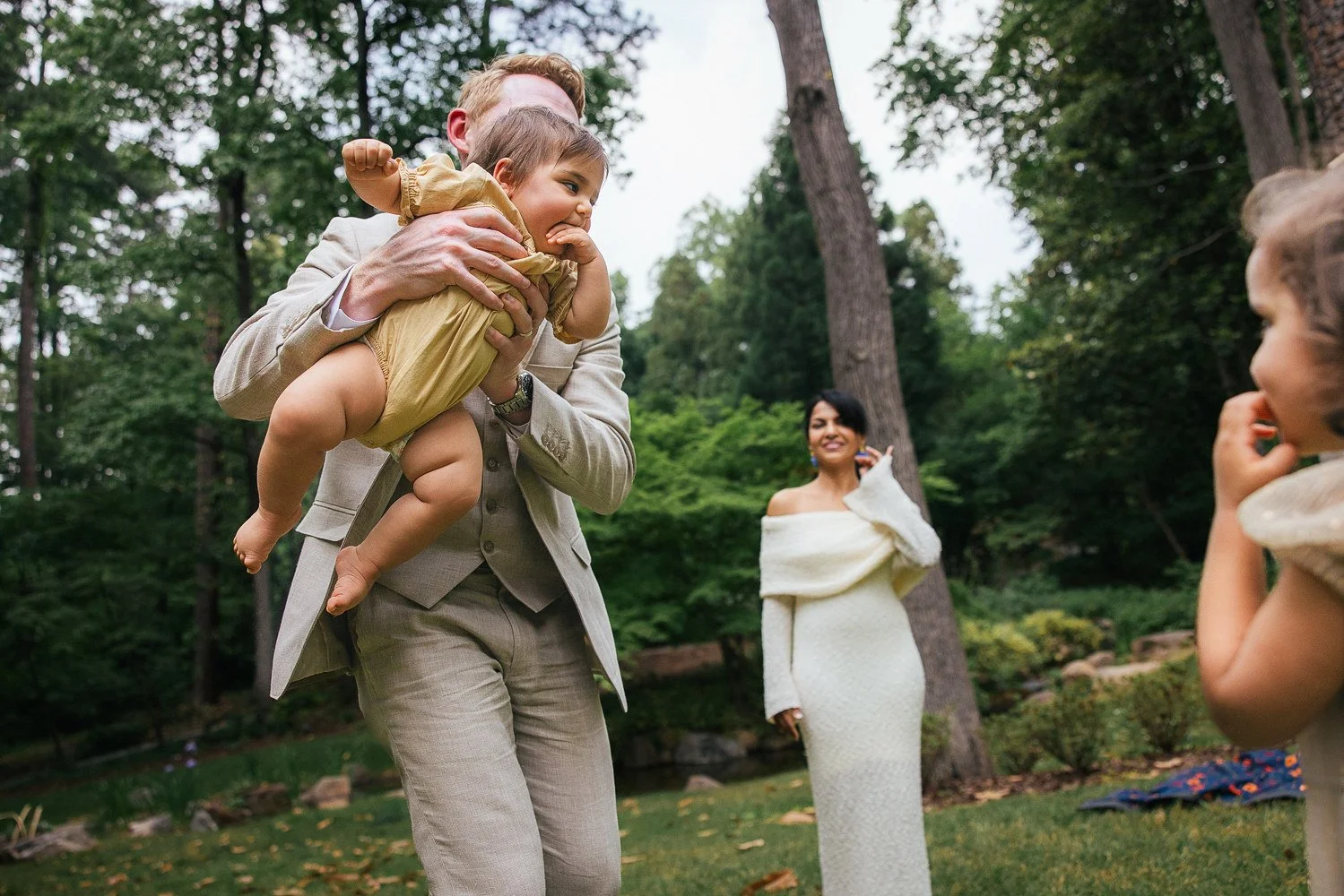 Father holds baby in a yellow onesie during a family photoshoot at Duke Gardens in Durham NC