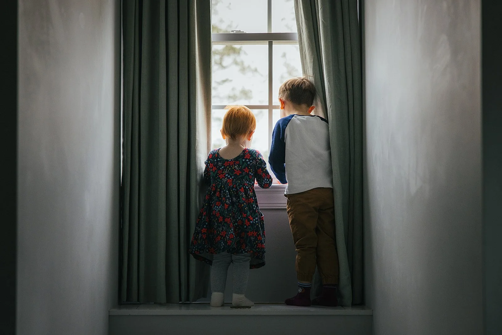 Two children look out a window during an in-home family portrait session