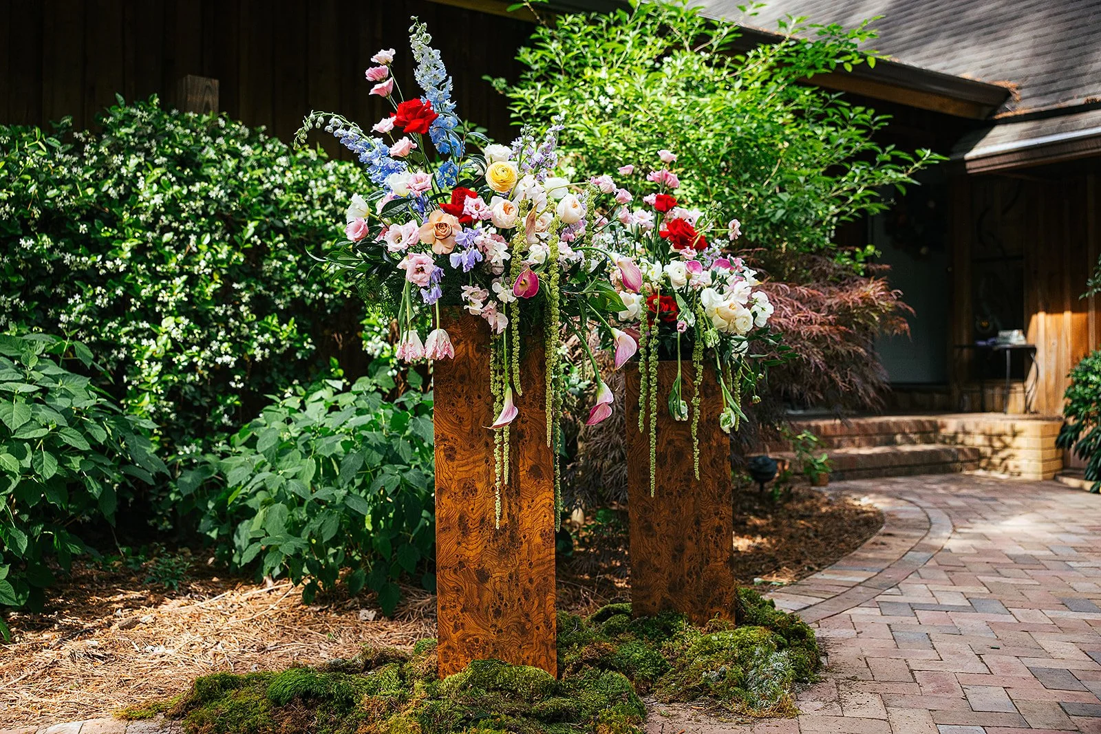 Three weathered rustic wooden ceremony pillars topped with lush colorful floral arrangements of roses, poppies, and trailing greenery, Durham NC wedding