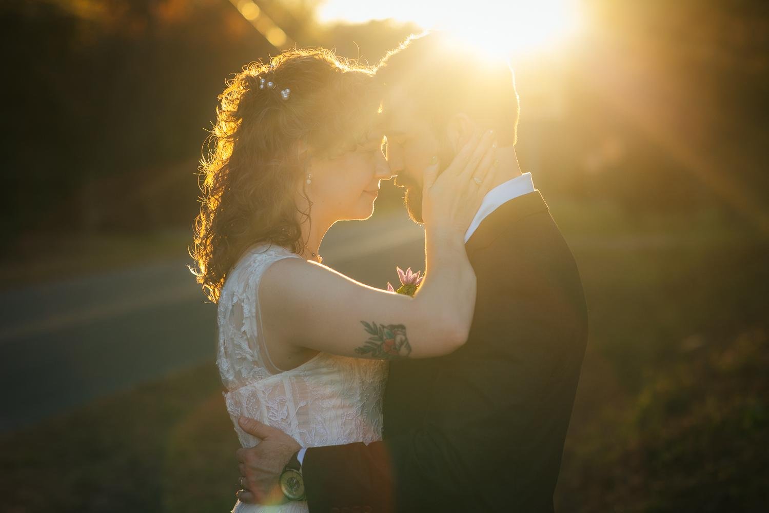 Bride and groom with foreheads together in a golden hour embrace — stunning sun flare — Honeysuckle Tea House wedding Chapel Hill NC — closing image