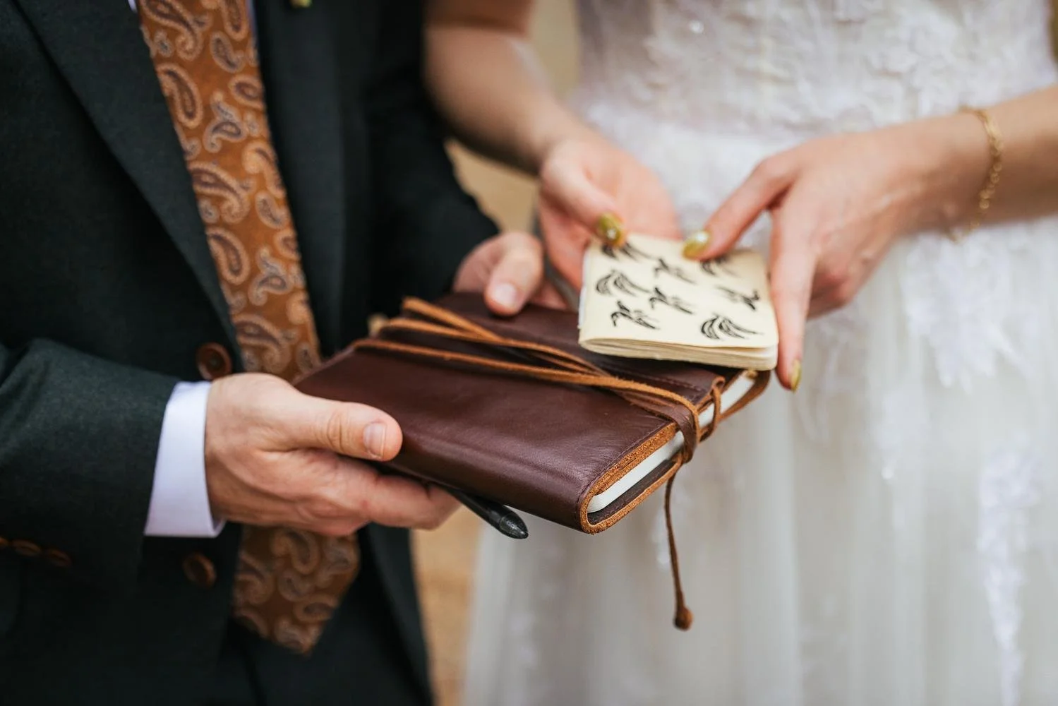 Close-up detail of groom holding a leather vow journal and bride holding a hand-illustrated booklet before their ceremony at Honeysuckle Tea House Chapel Hill NC
