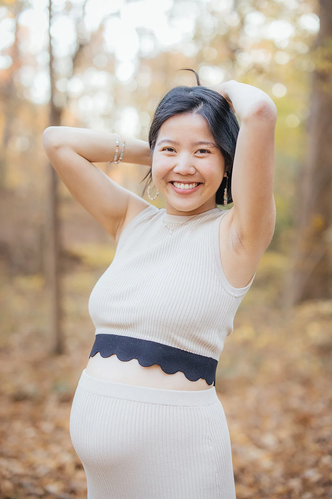 A pregnant woman smiles in a wooded area for a seasonal family photoshoot in Durham, NC