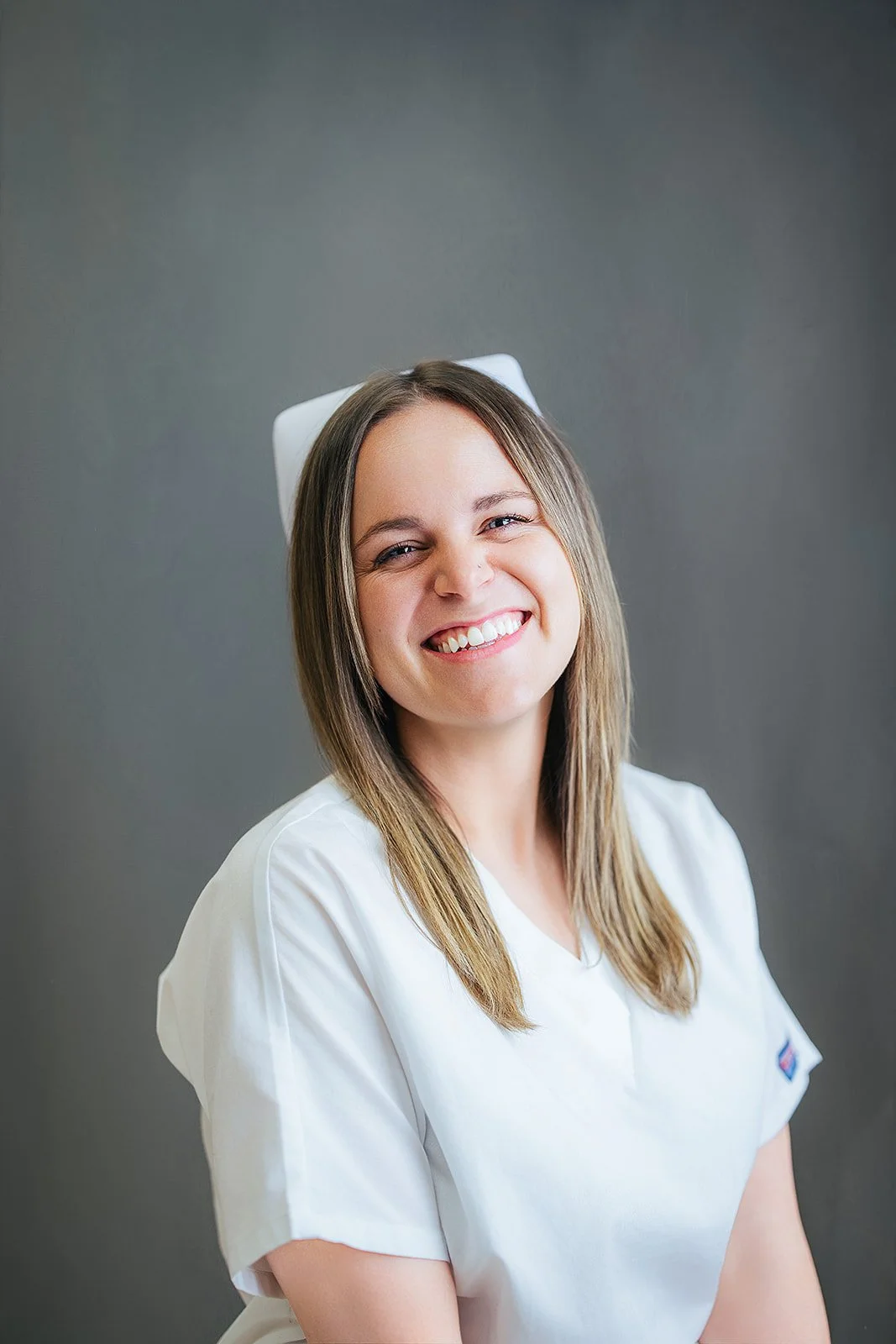 Durham Tech nursing student with long blonde hair and nurse cap, big bright smile in white scrubs, professional headshot in Durham NC