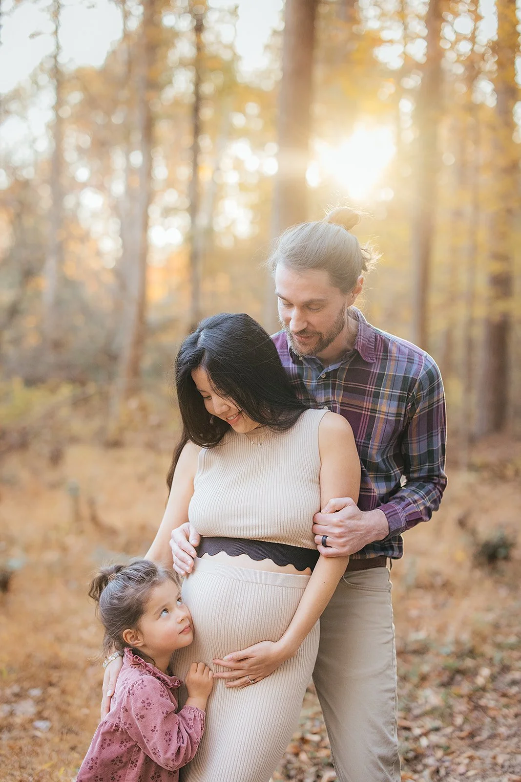 A pregnant woman poses with her family at a park for a Fall family photoshoot