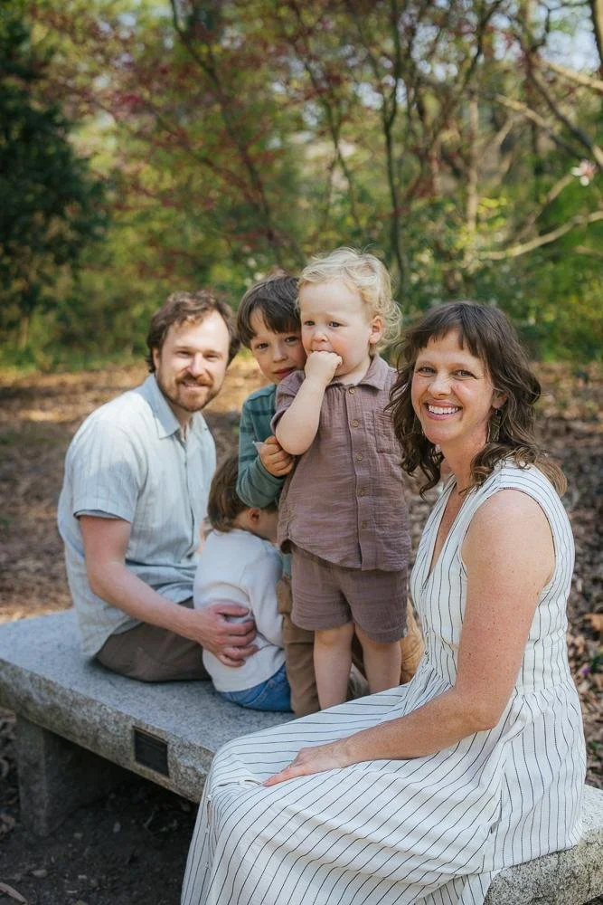 Family of five sitting together on a stone garden bench at Duke Gardens in Durham North Carolina — parents with three young boys