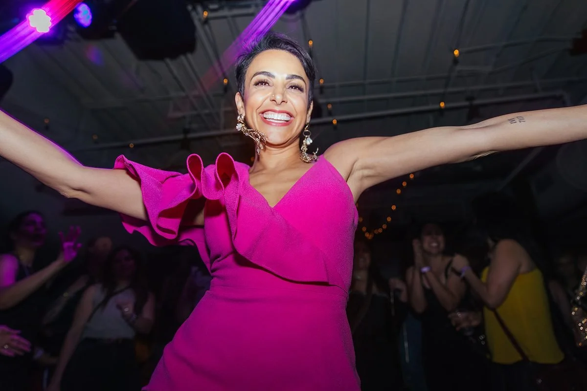 Woman in a hot pink ruffled dress with arms wide open and a radiant smile, dancing at the Dance Her popup at Transfer Co in Raleigh