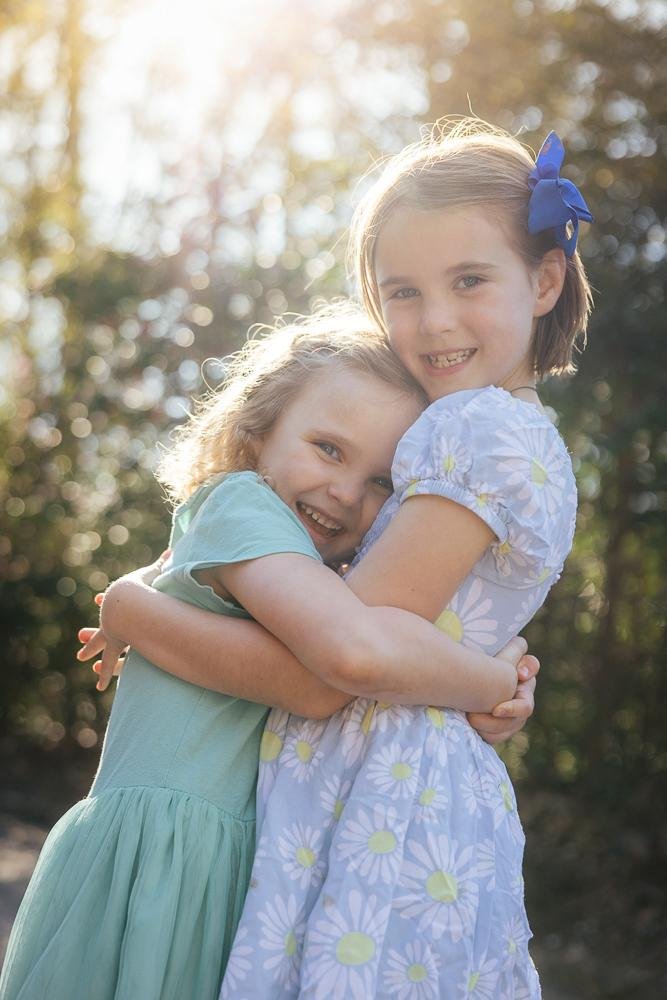 Two sisters hugging tightly with beautiful golden backlight during a family photo session at Duke Gardens Durham NC