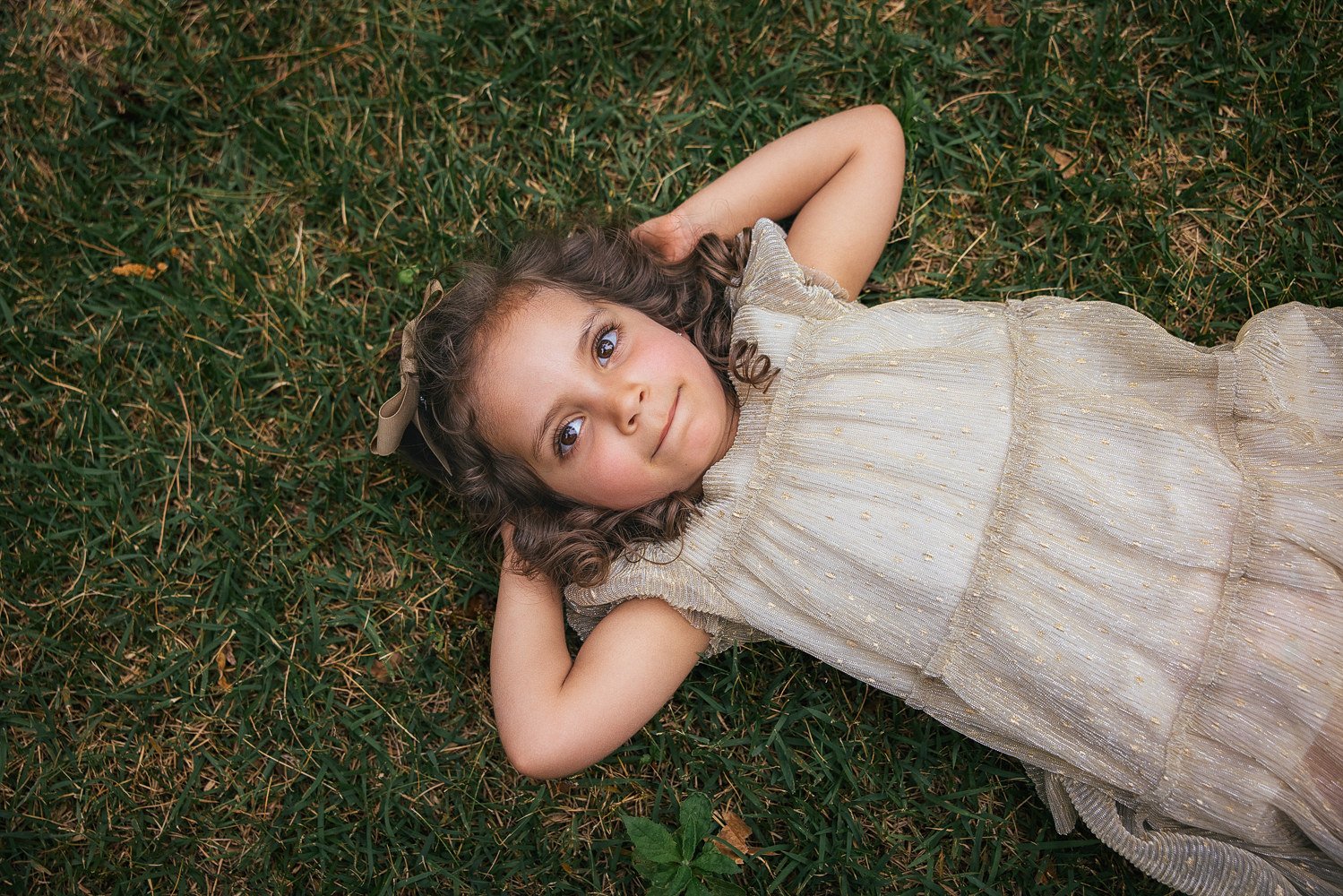 young girl with curly hair lays on a grassy lawn at Duke Gardens in Durham, NC for a family photoshoot