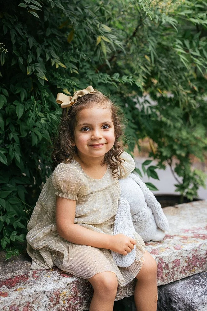 young girl poses with a stuffed animal on a stone wall in Durham, NC for a Duke Gardens photoshoot