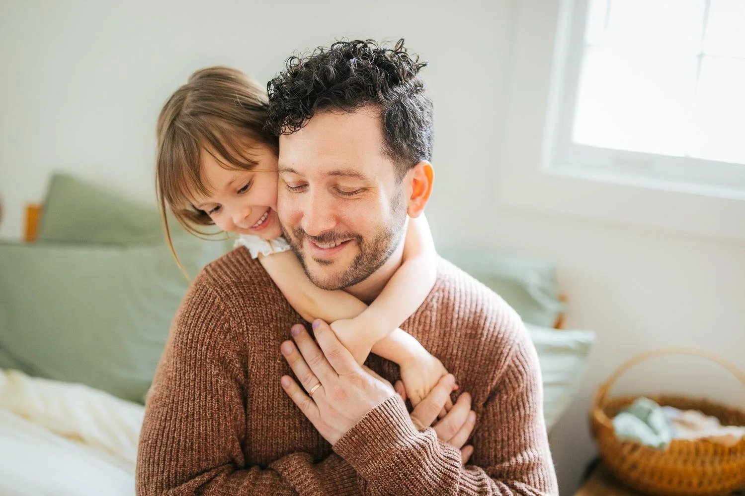 Dad smiling as his toddler daughter hugs him from behind during a Durham NC in-home newborn photography session