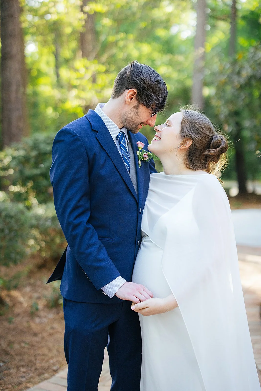 Bride and groom lean in forehead to forehead in dappled afternoon sunlight, eyes shining with joy, on a wooded path after their Durham NC wedding