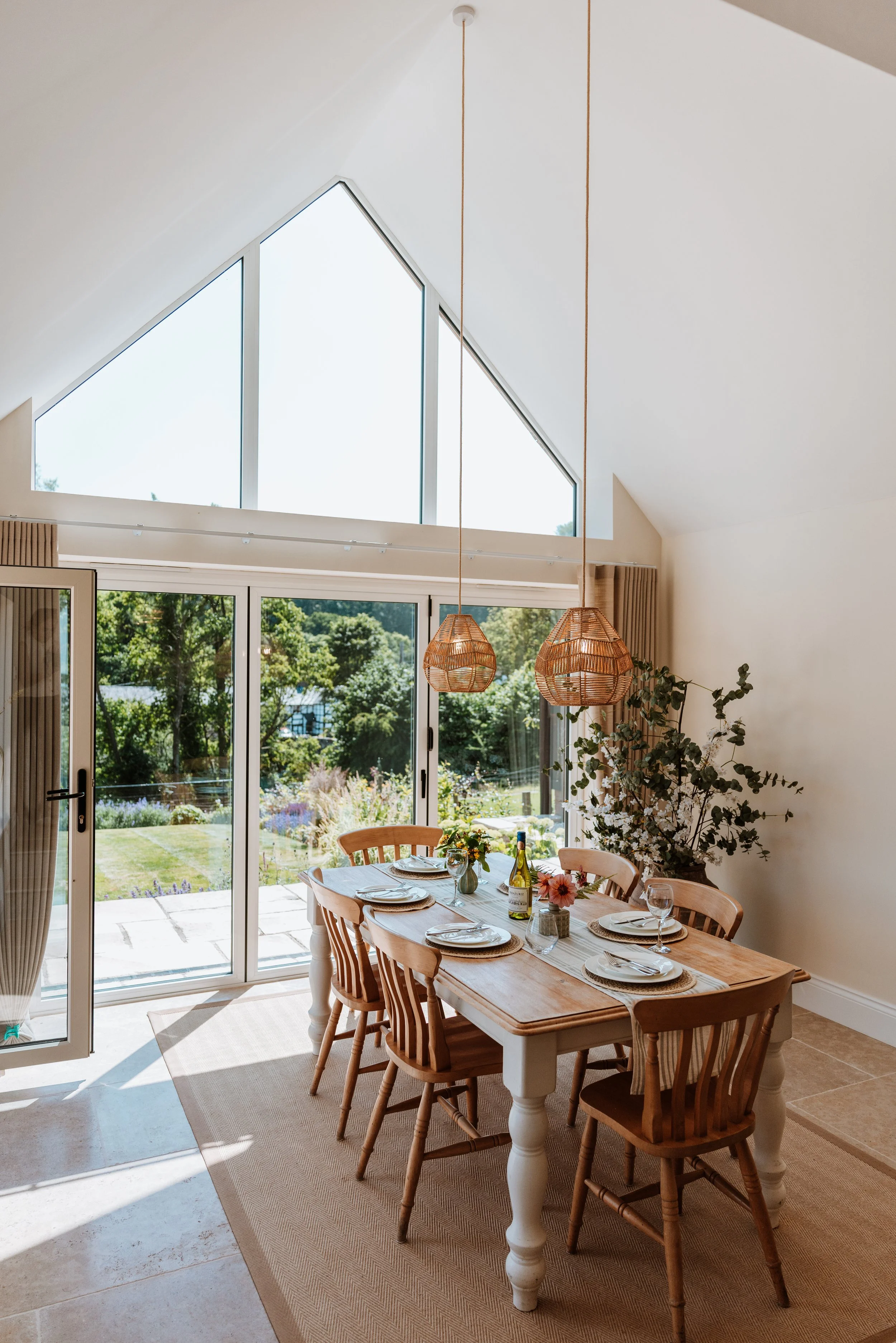 Dining room with wooden table, six chairs, set for a meal, large window, and outdoor garden view. Interiors by Lucy Rebecca Photography.