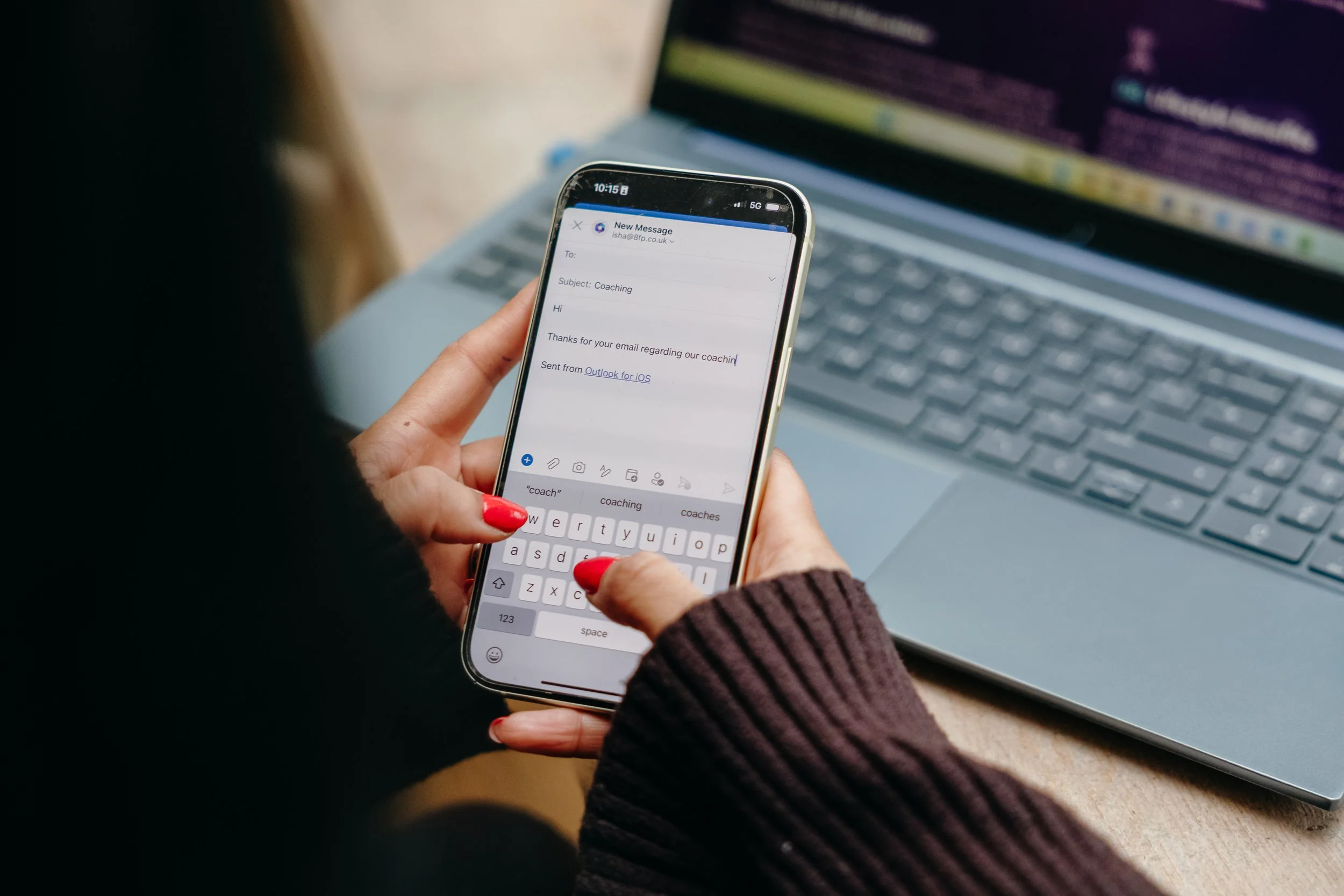 Person holding a smartphone with an email message on the screen, sitting in front of a laptop. Personal Branding by Lucy Rebecca Photography.