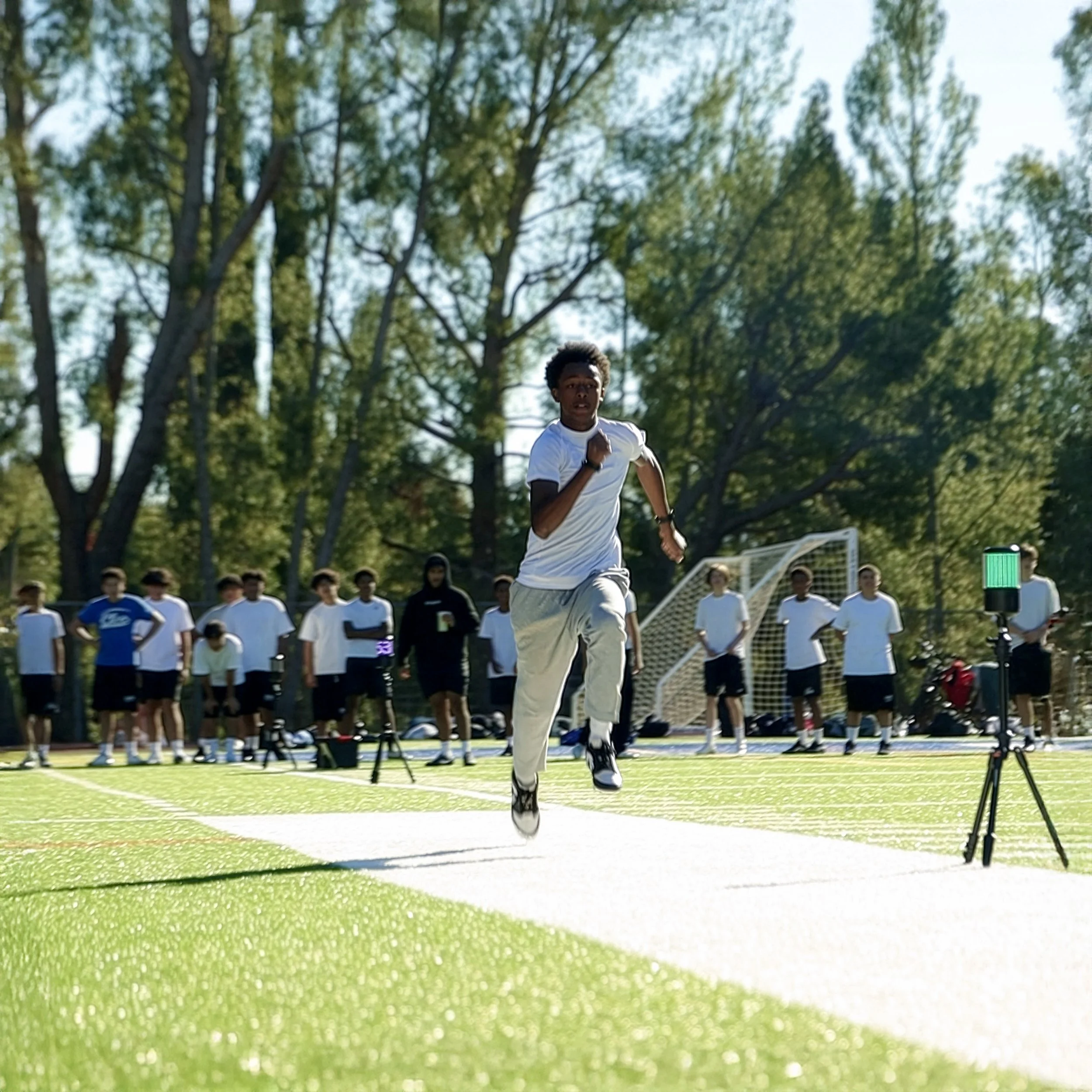 A young male athlete is sprinting on a track during a race, with a group of people watching in the background.