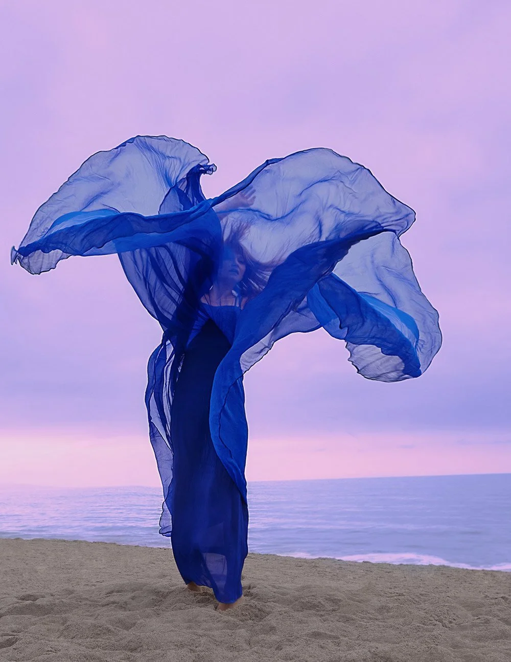 Beach portrait photography of a woman in graceful movements, styled in light violet and indigo. Colorized, translucent layers, bold colors, and theatrical gestures create a captivating scene. Ideal for personal branding and photoshoots
