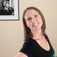 Smiling woman wearing a pink scarf and top with a black and white framed photo in the background.