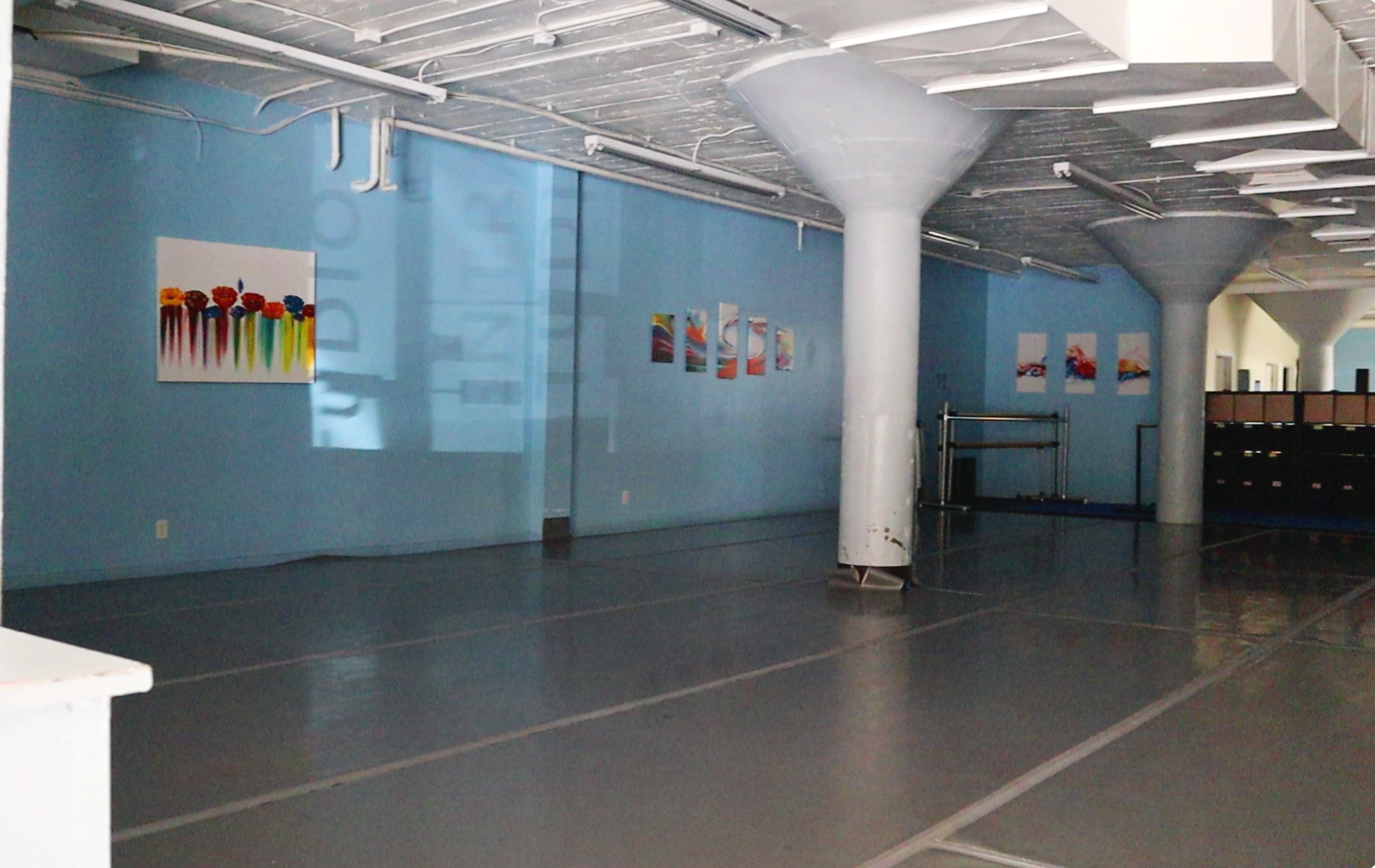 Empty indoor sports or community center with blue walls, colorful paintings, and structural white columns.
