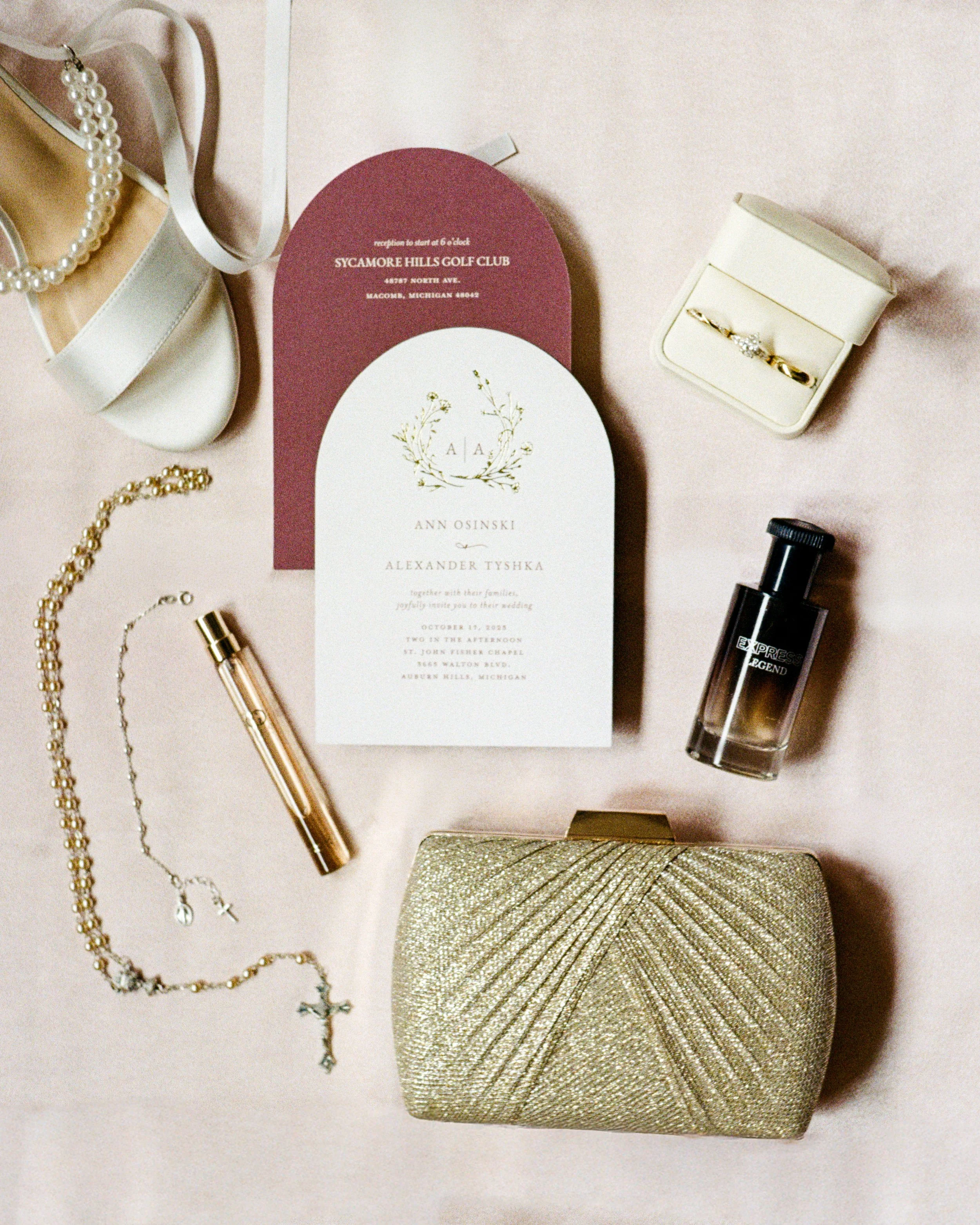 Wedding invitation, jewelry, perfume, makeup, and accessories arranged on a soft pink surface.