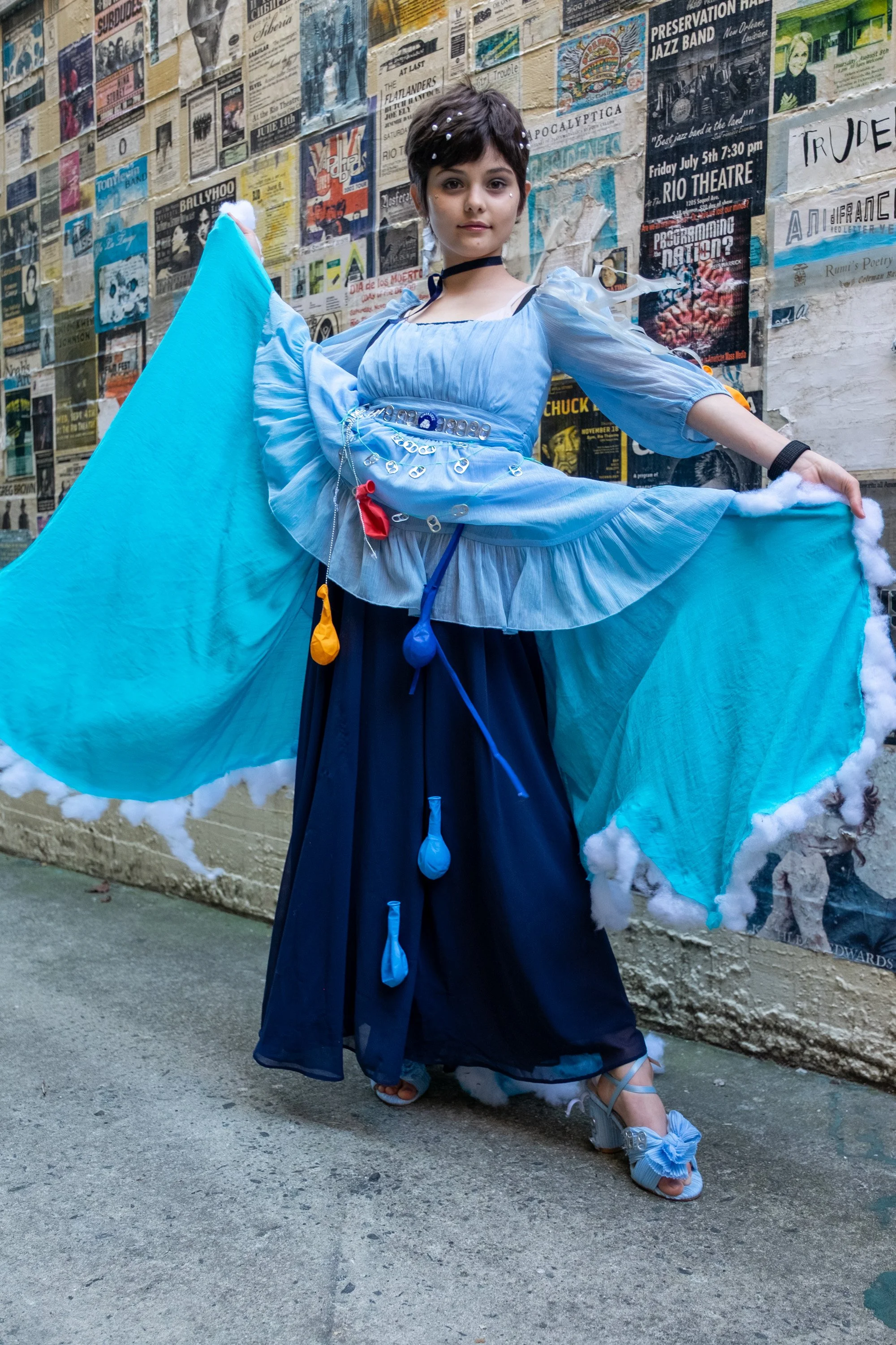 FashionTeens Santa Cruz student wearing an upcycled satin dress with tulle and embellishments, carrying an umbrella covered in twinkle lights for a magical, ethereal runway look