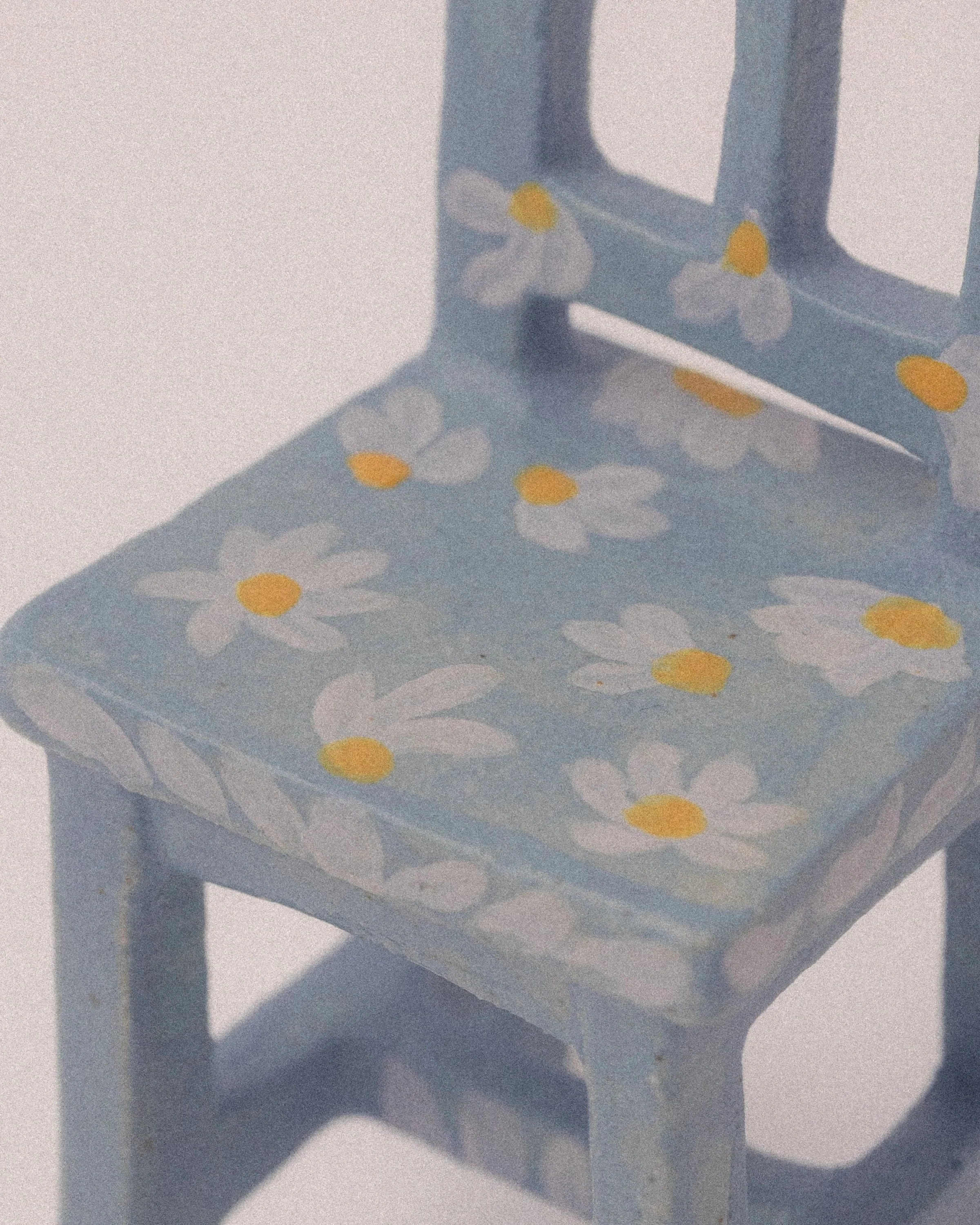 Close-up of a light blue ceramic tiny chair sculpture with a white daisy flower design, against a white background