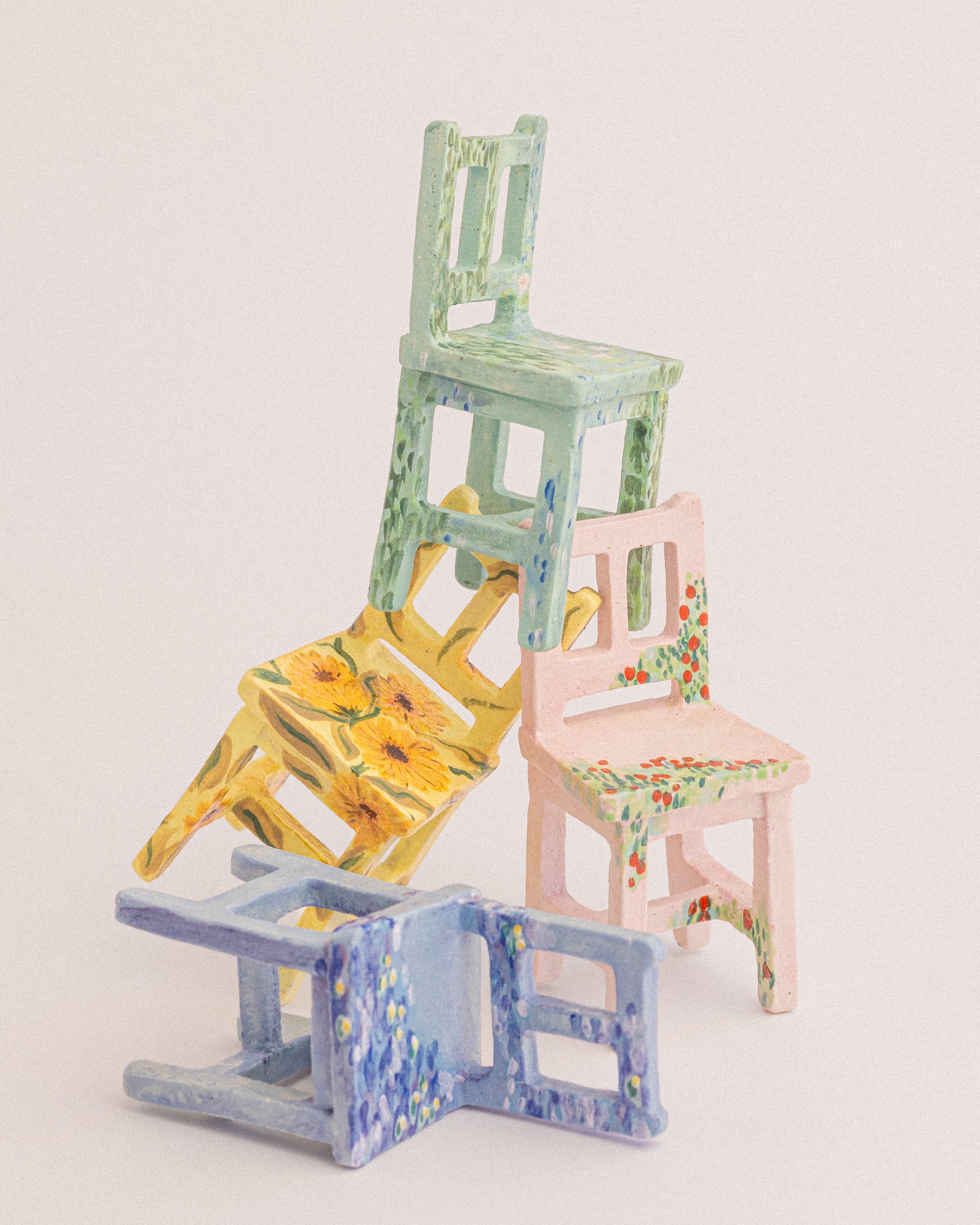 tiny ceramic chair sculptures in pastel colours with floral motifs painted on the surface stacked into a pile on a plain white background