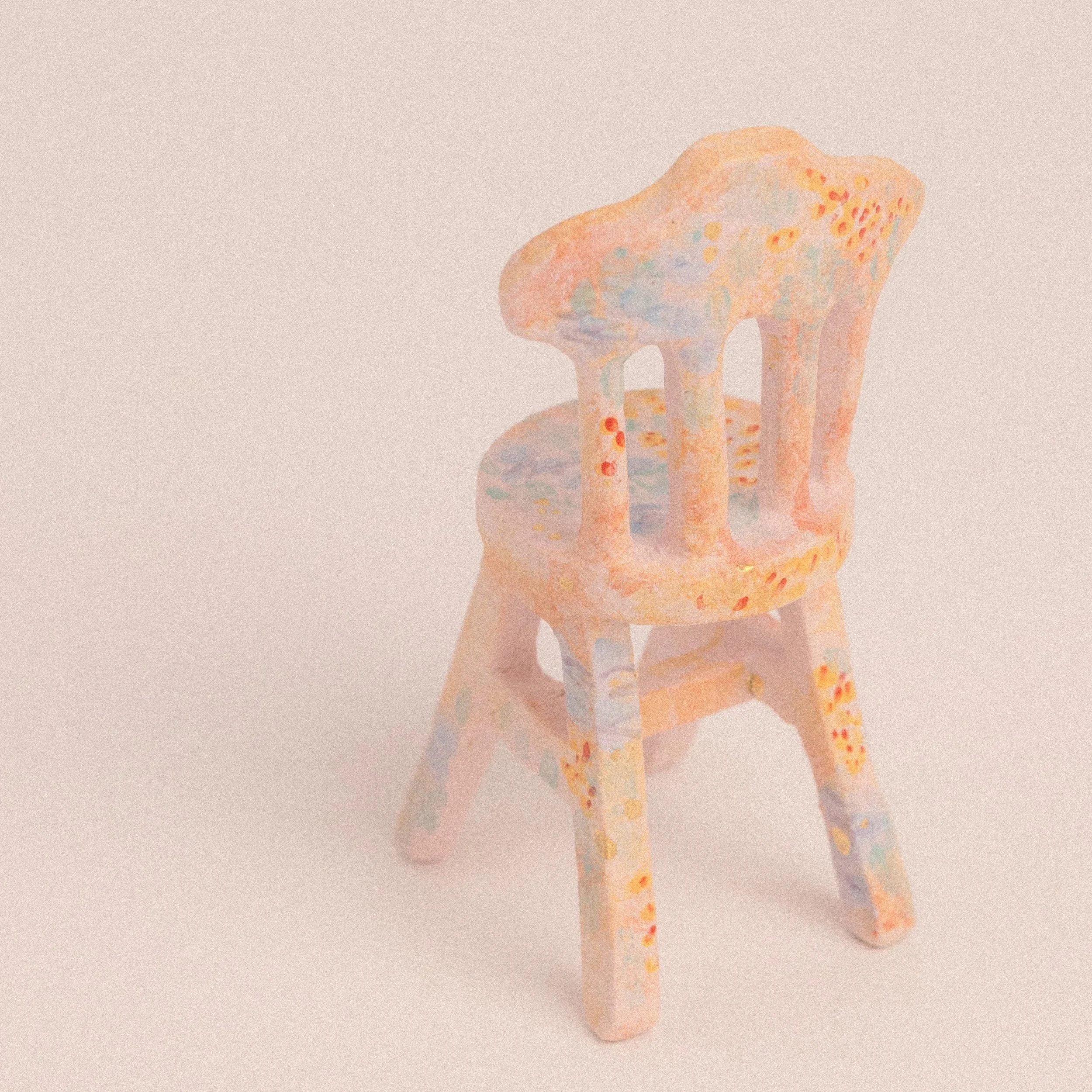 tiny ceramic chair sculpture in pastel colours facing away from the viewer against a plain soft pink toned background
