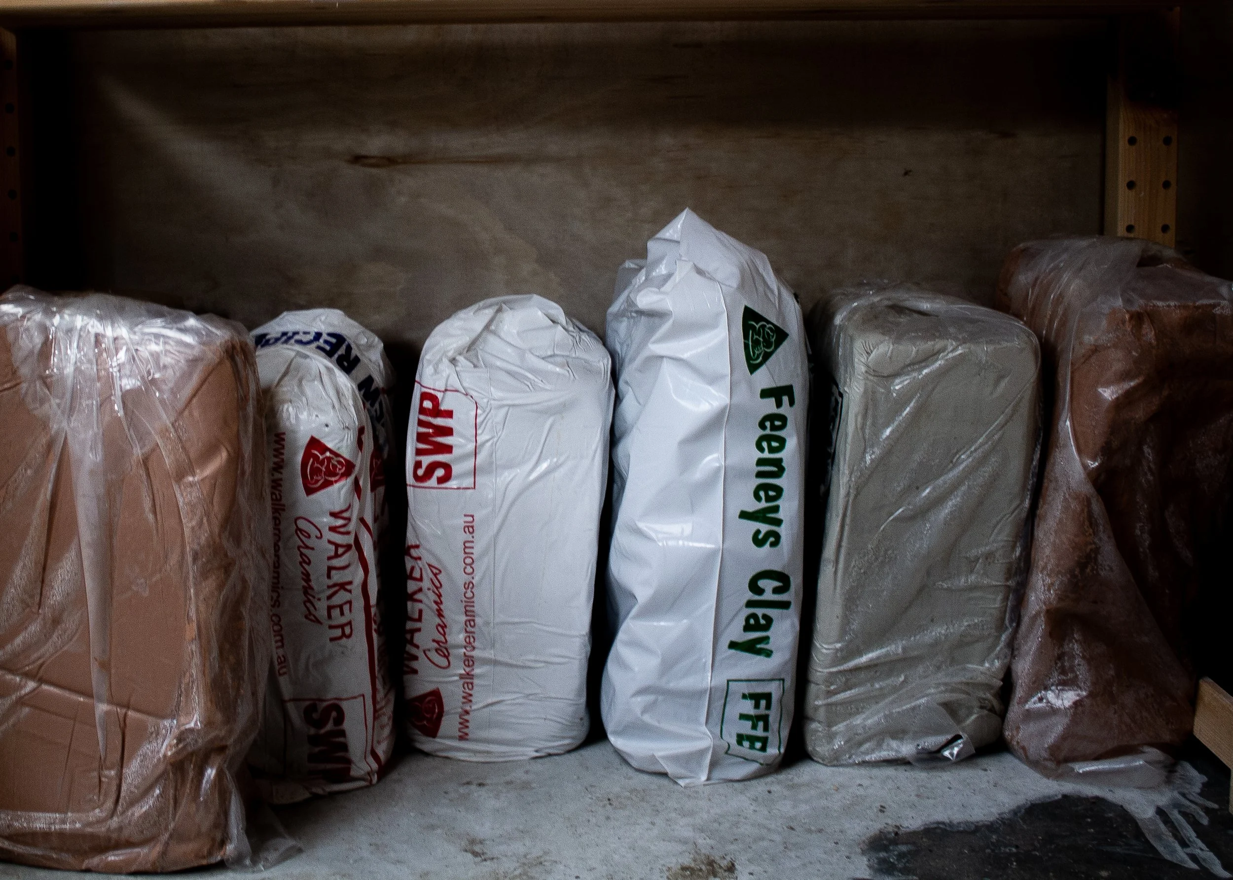 Bags of different stoneware coloured clay lined up next to each other in a row on the floor of the home pottery studio of Melbourne based ceramic artist Emily Brookfield