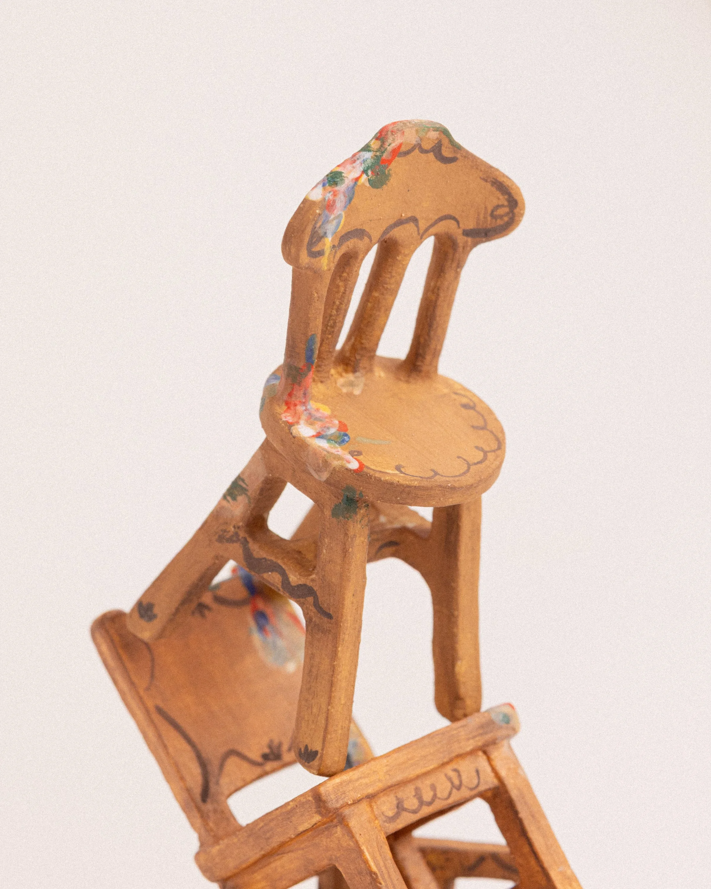 two brown ceramic miniature chair sculptures stacked on one another with a wooden look and paint splatters against a plain white background