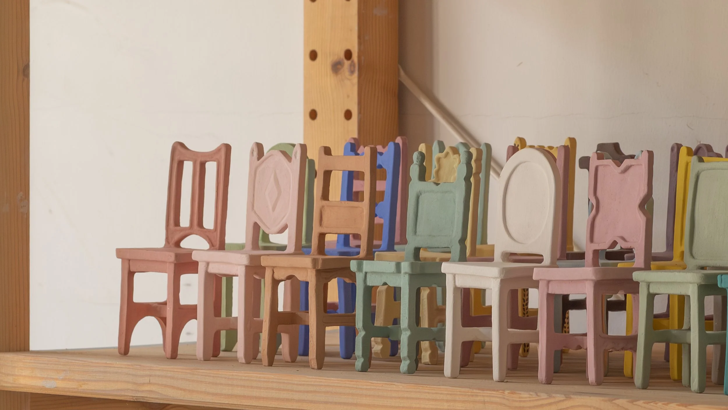 Miniature ceramic chair sculptures in pastel colours sitting on a shelf in the pottery studio of Australia ceramic artist Emily Brookfield