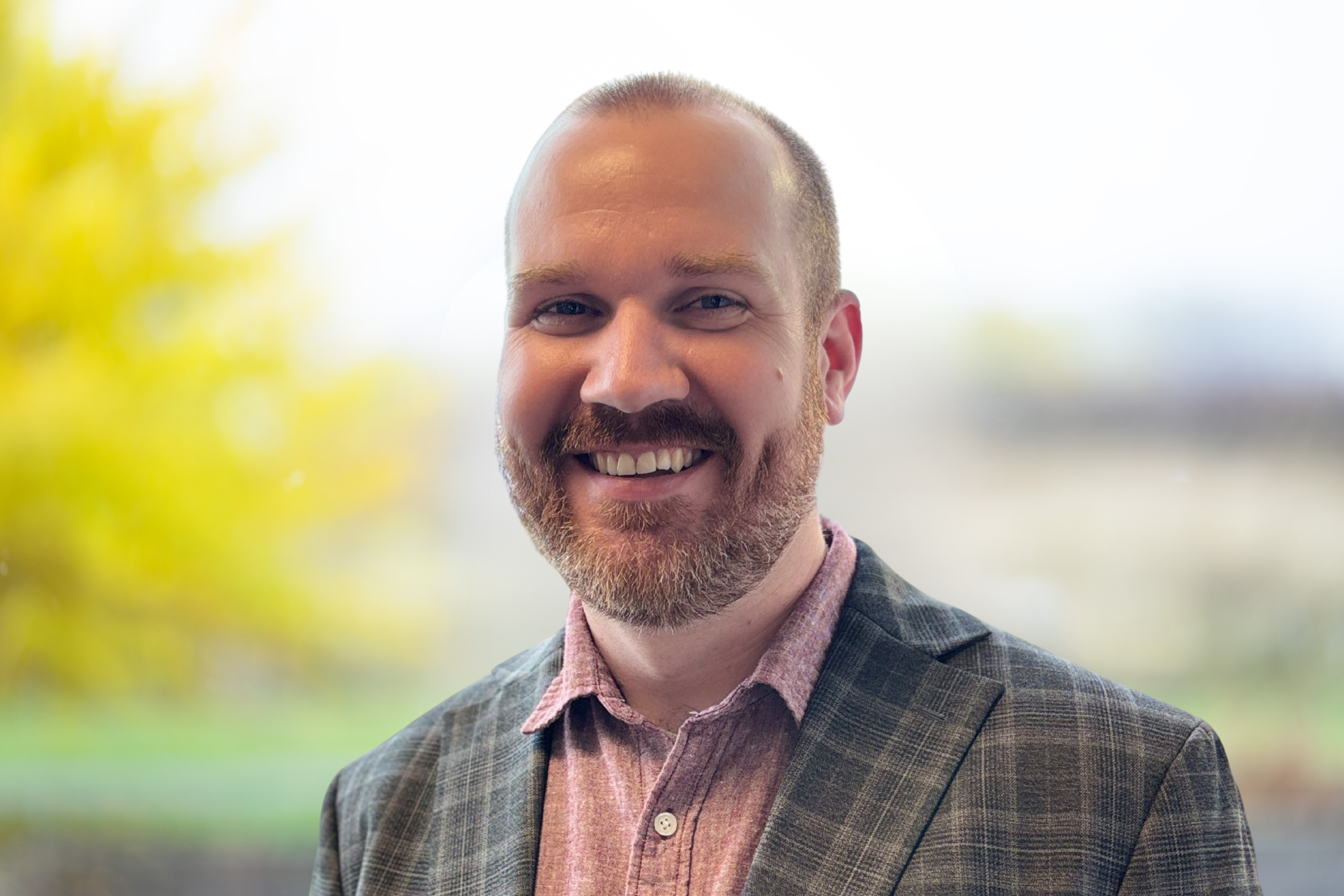 Portrait of Collectivfide CFO, Rick, smiling in business attire, blurred outdoor background with greenery.