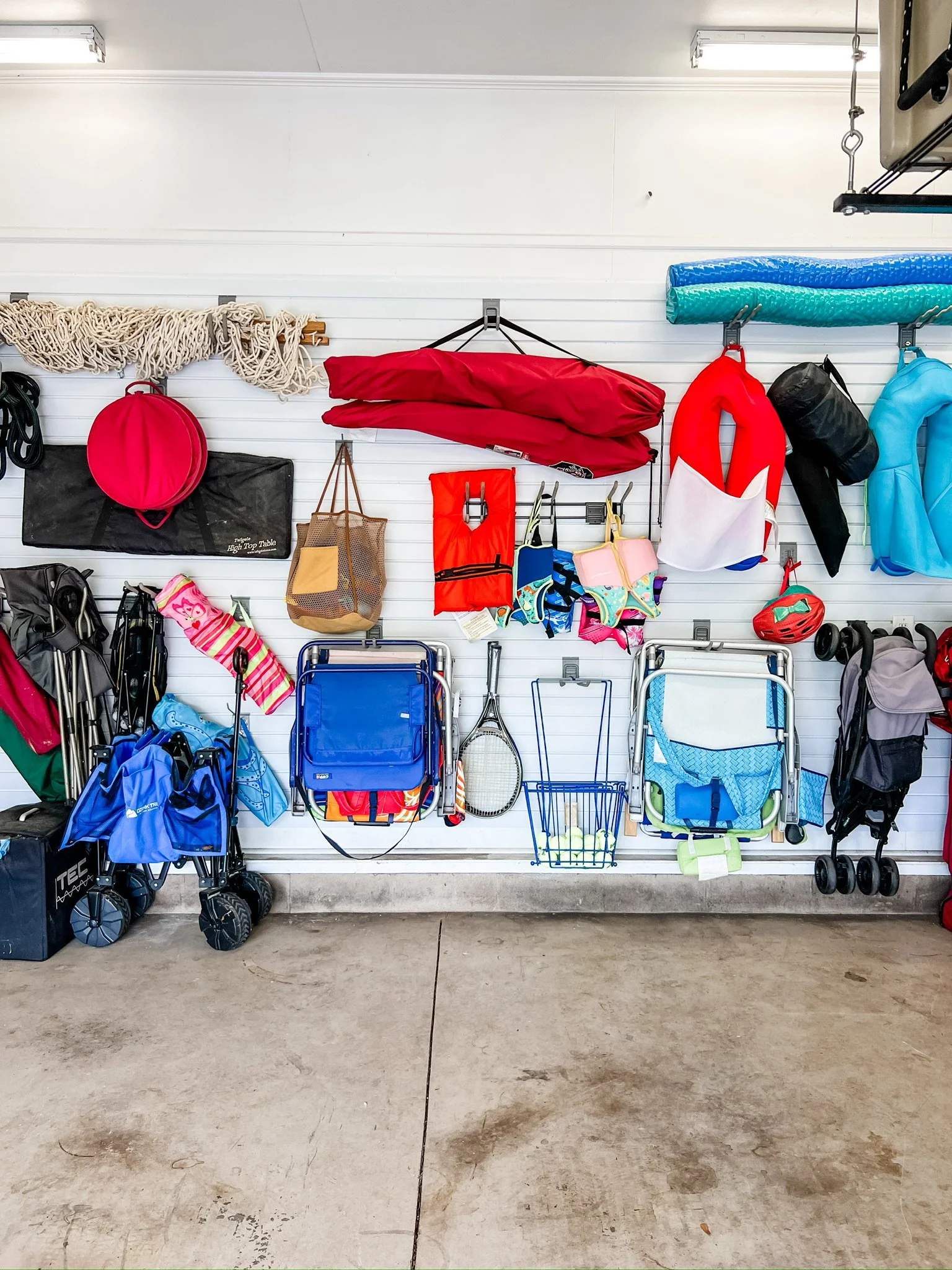 Garage wall with beach chairs, umbrellas, bags, and summer gear neatly organized on wall hooks.