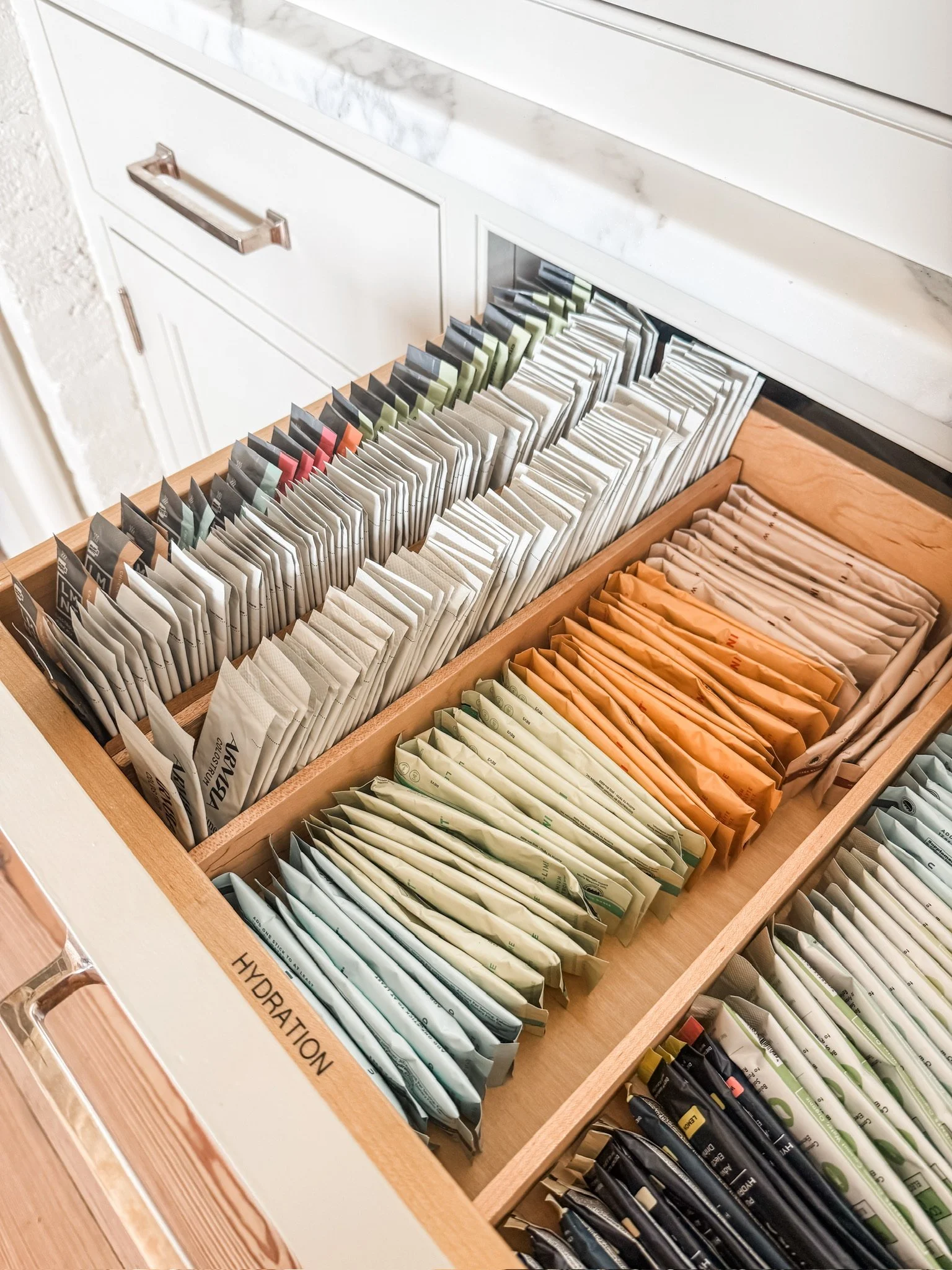 Organized kitchen drawer with electrolyte packets, drink mixes, and hydration supplies neatly separated in storage organizers.