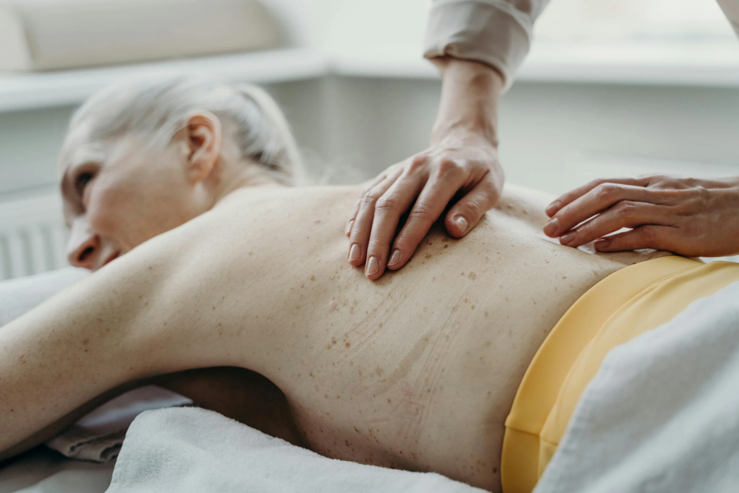 A person receiving a back massage from a massage therapist in a bright, clean room.