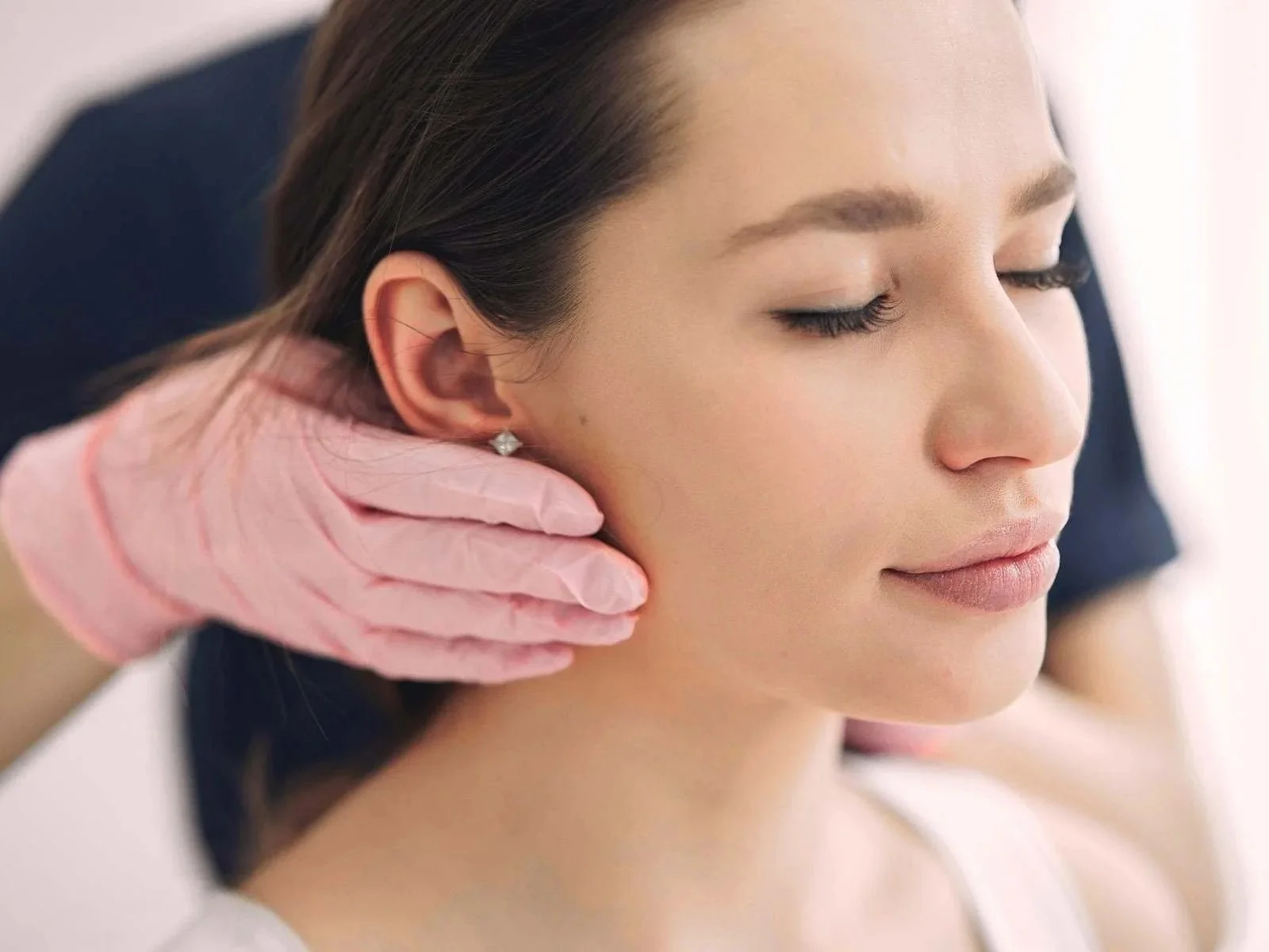 a practioner wearing pink medical gloves accessing a womans jaw area