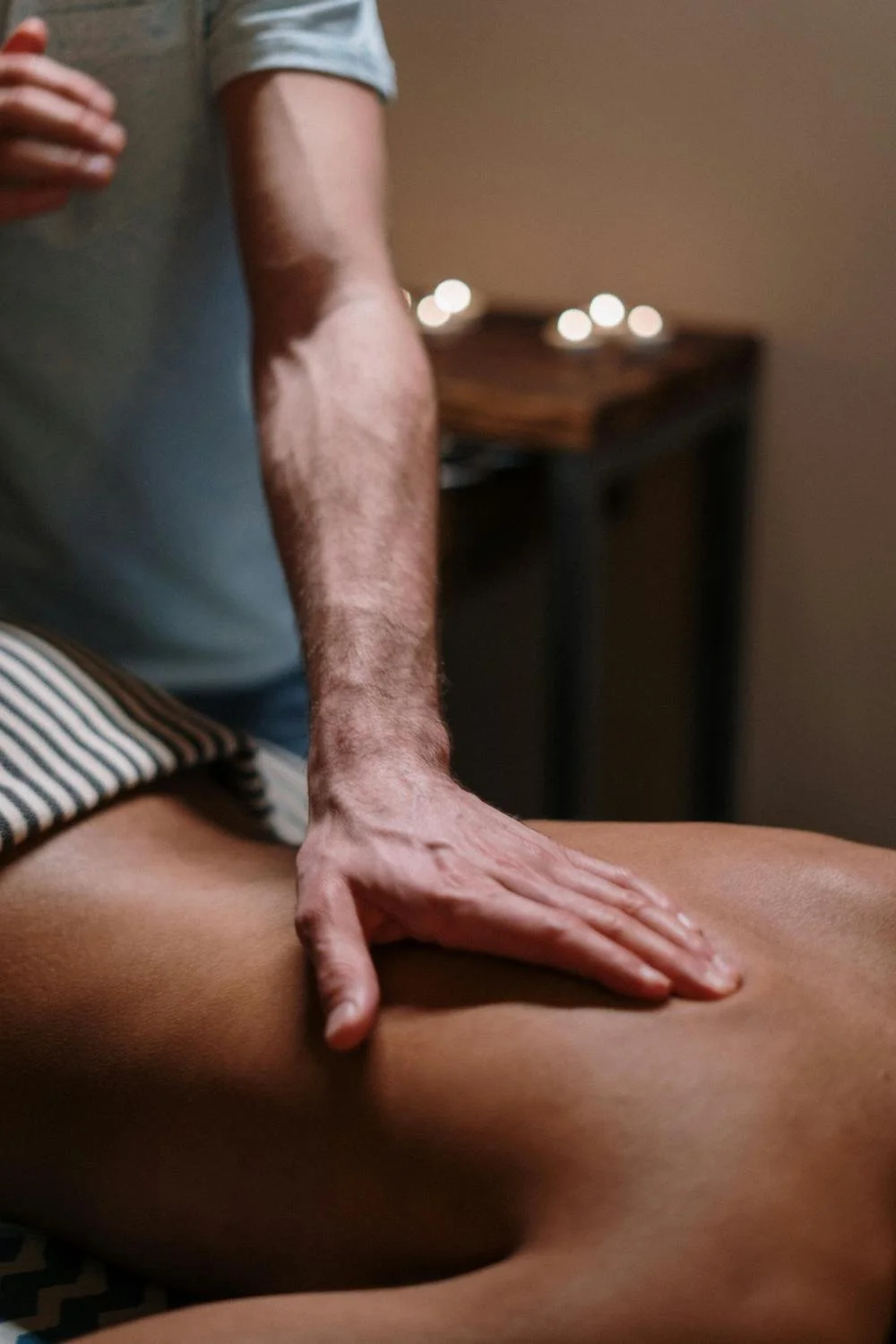 Close-up of a person giving a massage to another person's back in a dimly lit room.