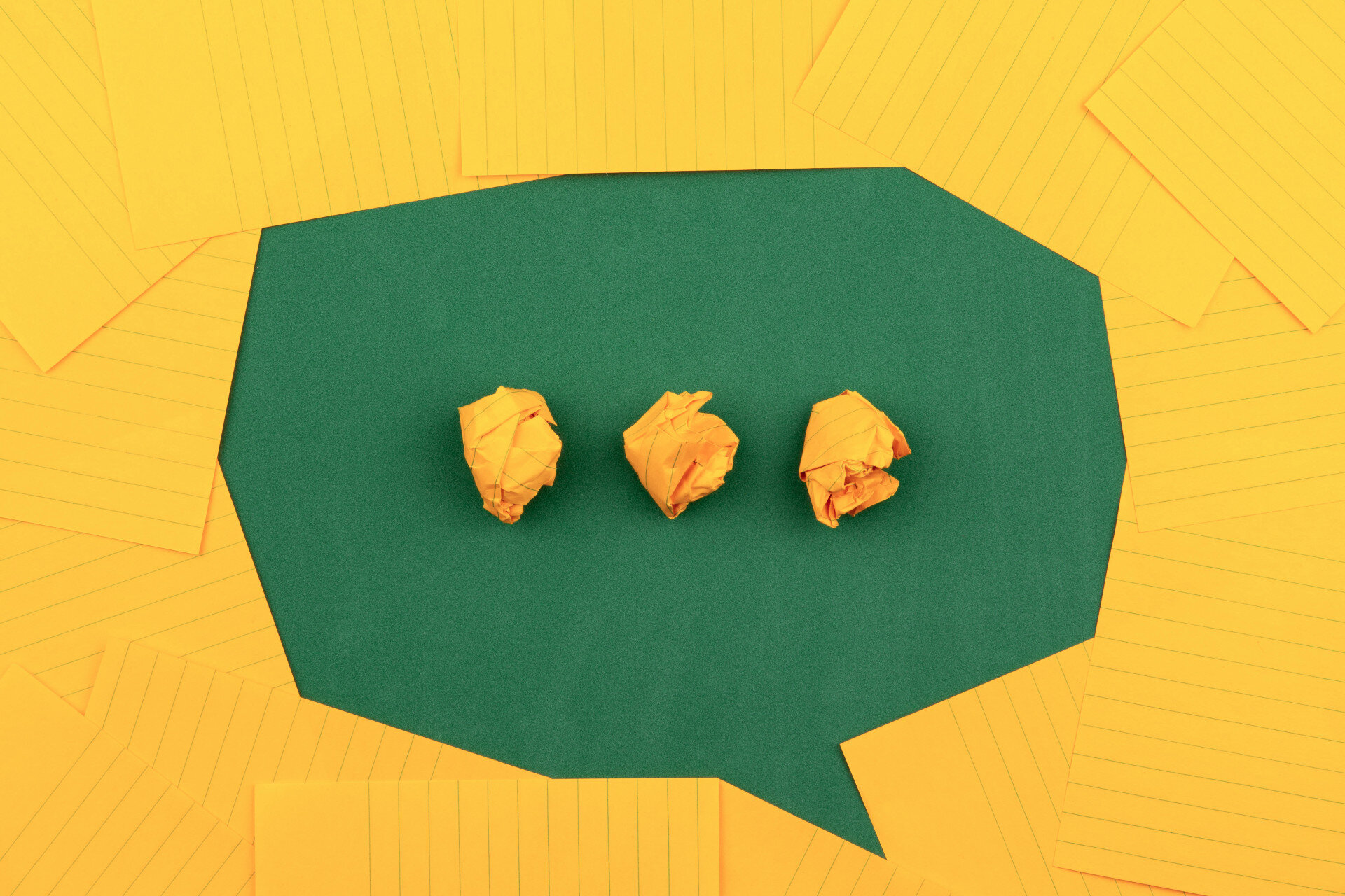 Stock photograph by Volodymyr Hryshchenko. Image ID: orange sheets of paper on top of green construction paper form a chat bubble with three crumpled orange balls of paper to suggest that someone is preparing to say something.