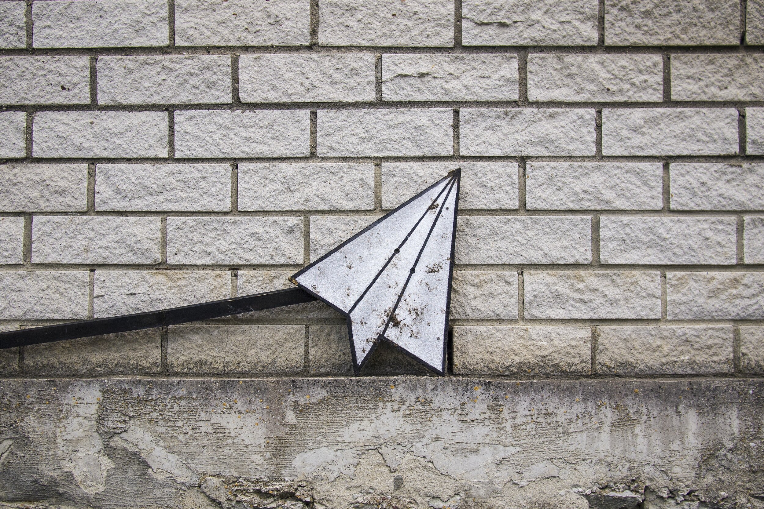 Image: This piece of street art is a sculpture that looks like a paper airplane or the symbol for a DM on Instagram. It’s propped up against a white brick wall with the nose facing upward, like a message waiting to be sent.