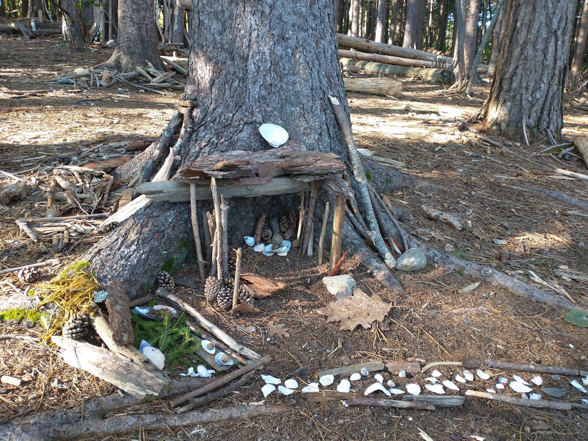 The bottom of a tree trunk that's been fashioned into a fairy house with sticks for a doorway and a pebble path.