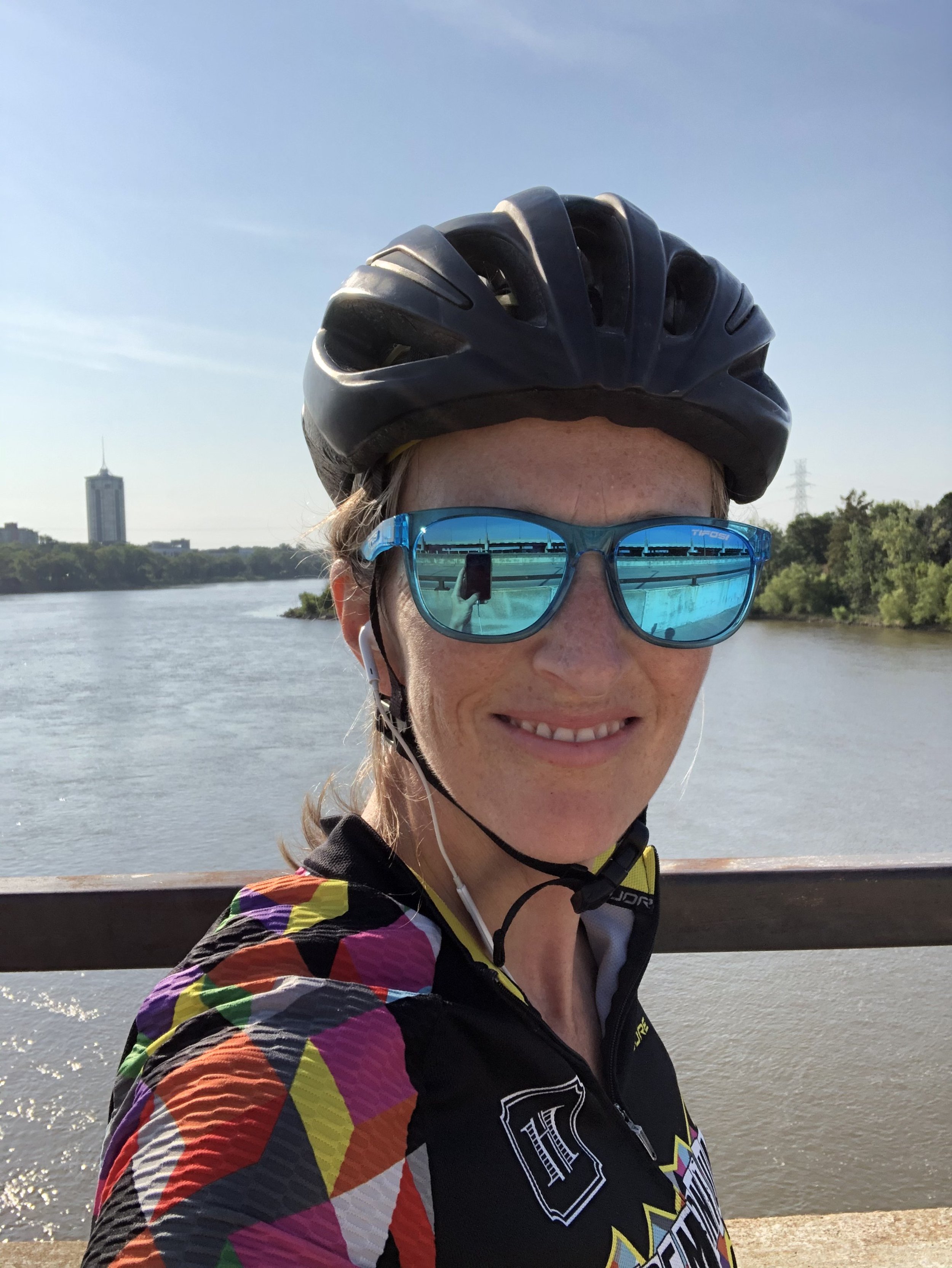 Person wearing a helmet and sunglasses, standing on a bridge with a river in the background.