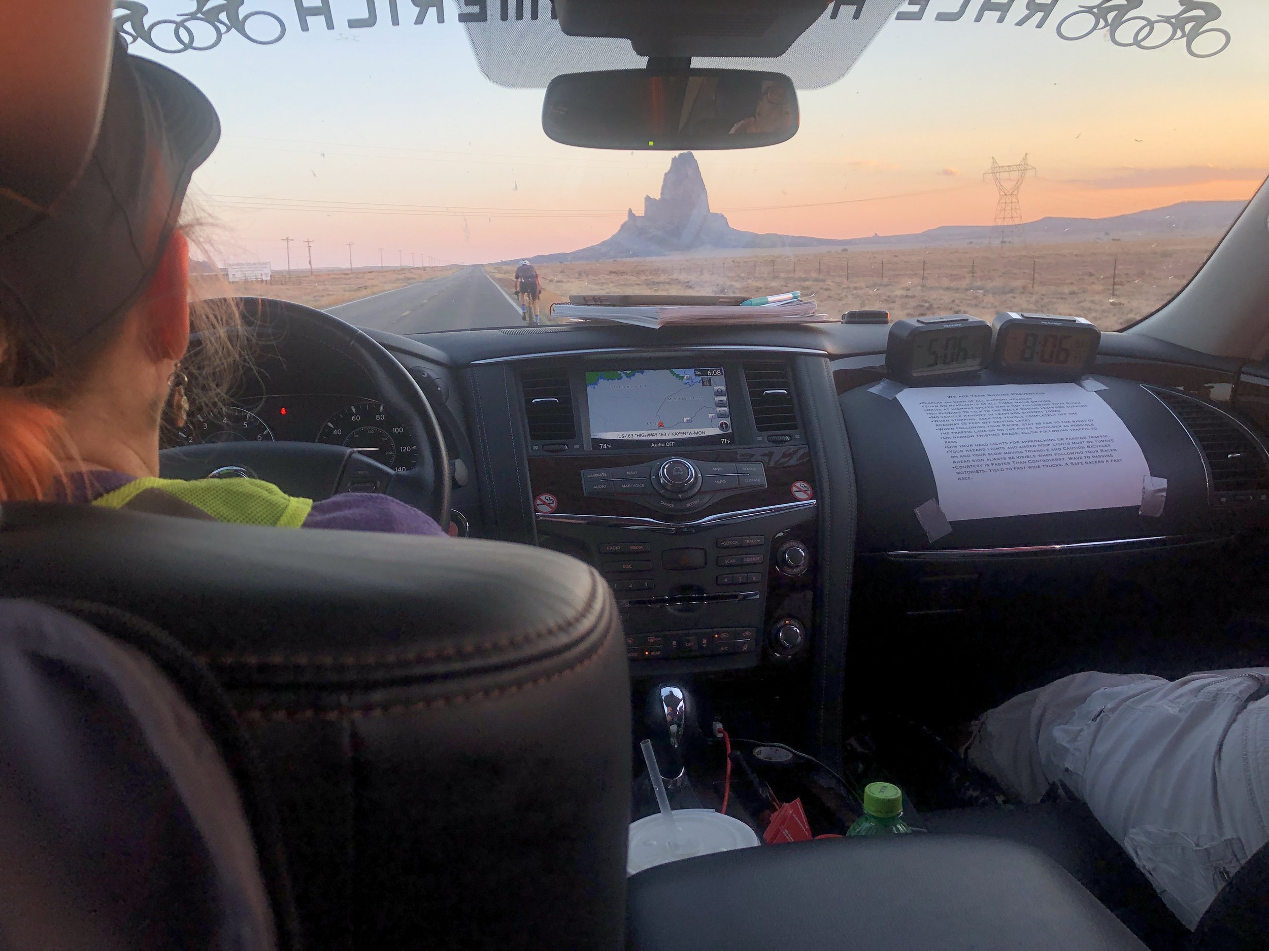 Inside a car, dashboard view with GPS navigation, cyclist on the road in the distance, monument in the background.