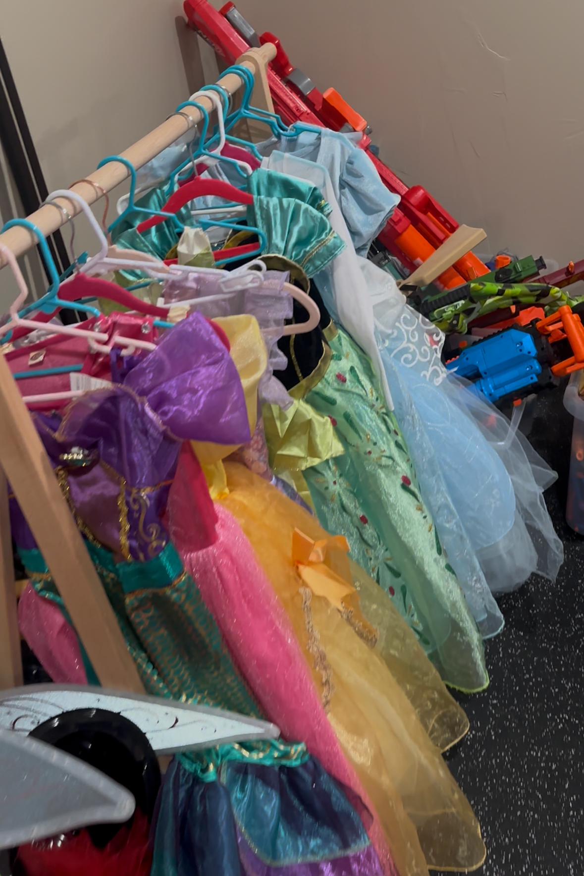 Organized playroom dress‑up area with colorful costumes hanging on a wooden clothing rack and toy accessories neatly arranged beside it.