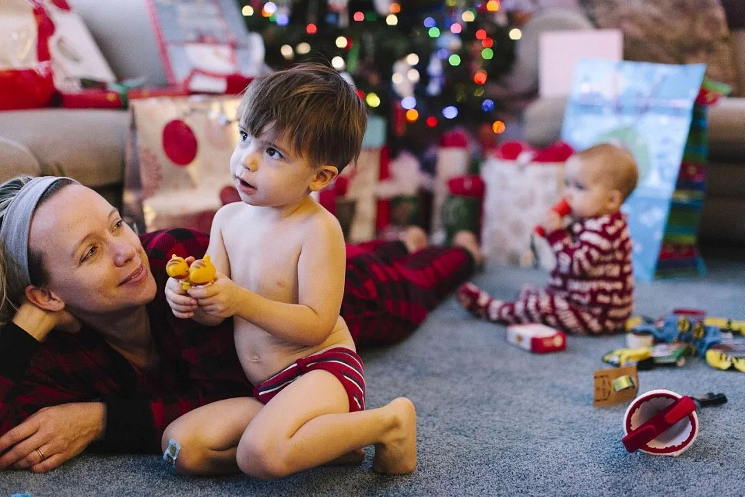 Toddler family Christmas photo by the tree and gifts, capturing intentional holiday memories in a slow storytelling style.