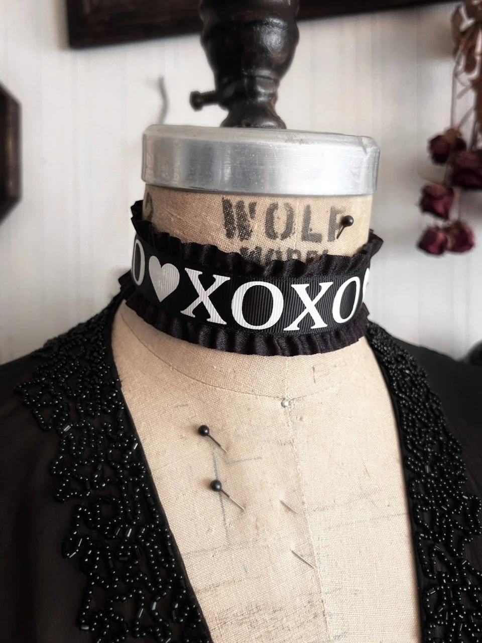 1.5 inch wide black satin ruffle edge choker collar necklace with XOXO flanked by hearts printed at center front in bold white letters. Romantic goth dark fashion Valentine's Day
