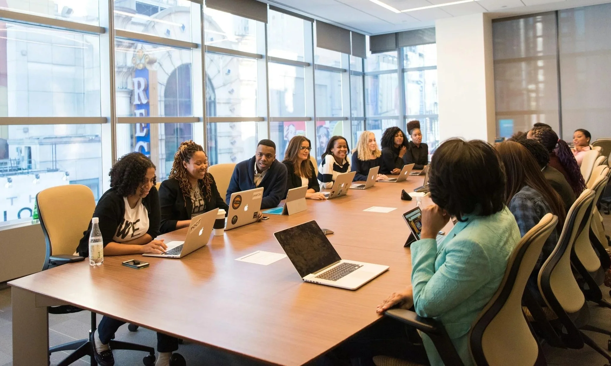 A diverse group of professionals having a meeting around a large conference table in a modern office with floor-to-ceiling windows.